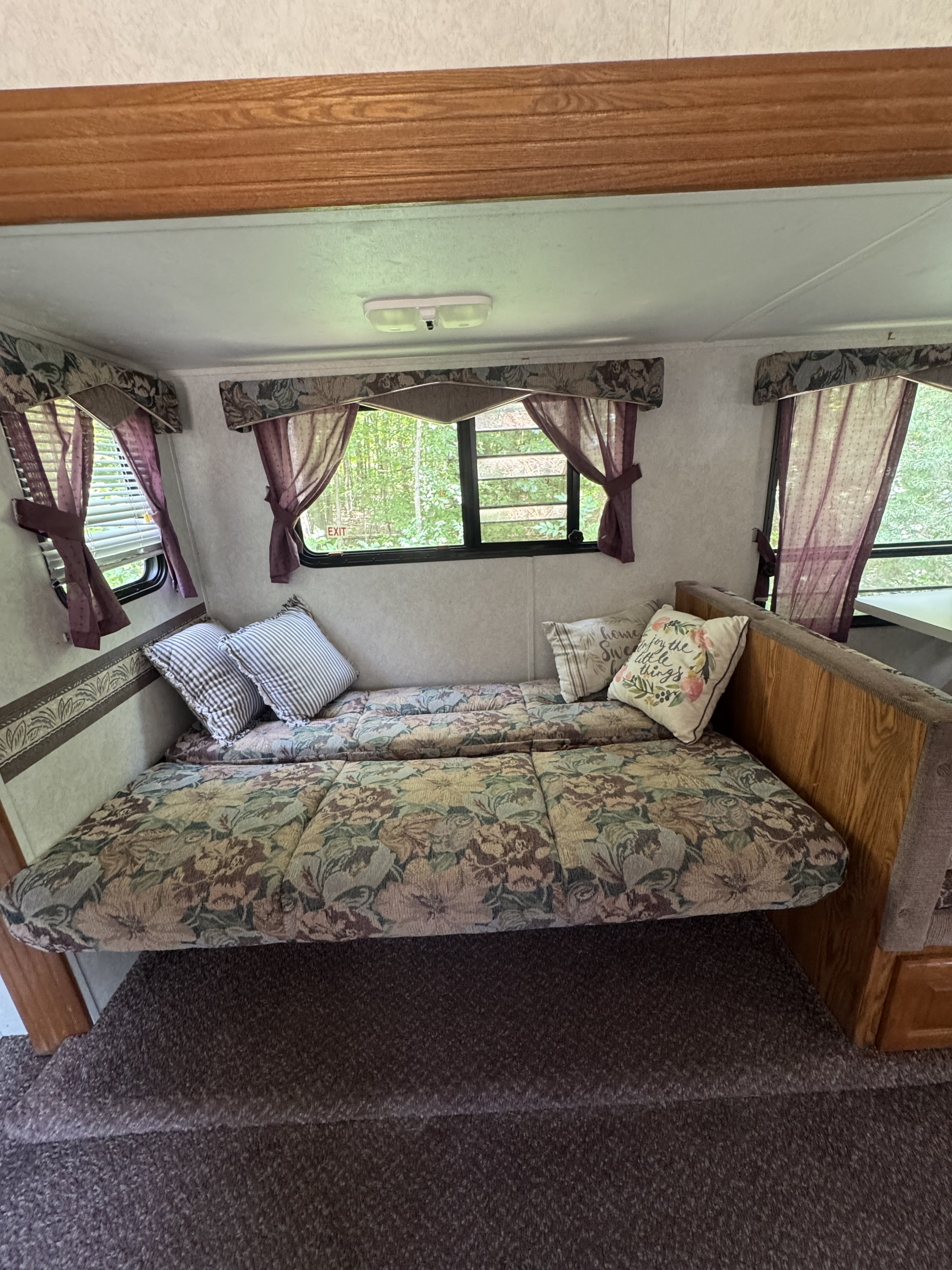 Cozy RV rental interior showing a floral-patterned seating area converted into a bed with windows and decorative pillows.. Forest River Wildwood 2000