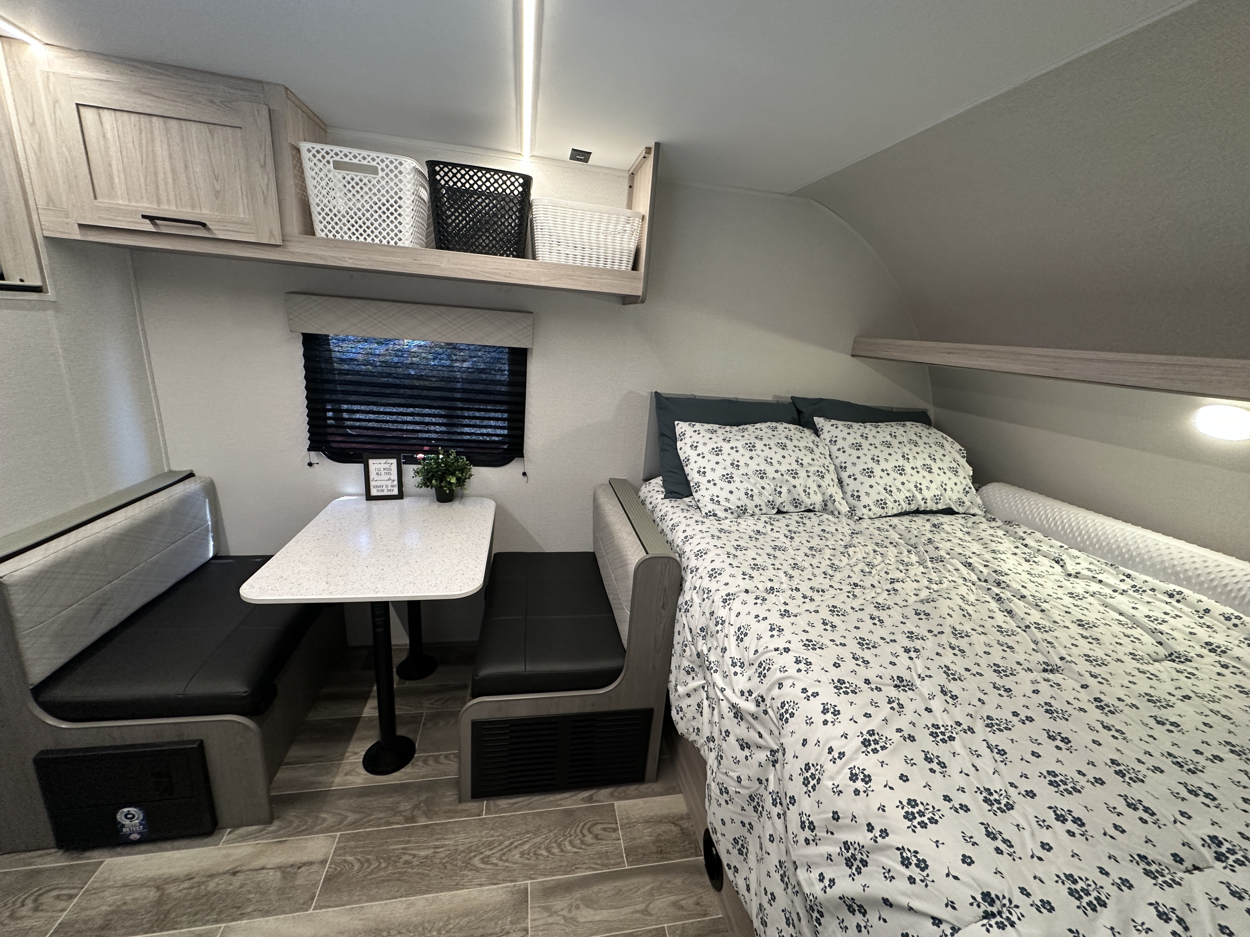 Cozy RV rental interior featuring a compact dining area with a table and bench seating, plus a comfortable bed with floral bedding.. Heartland Mallard 17bhl 2025