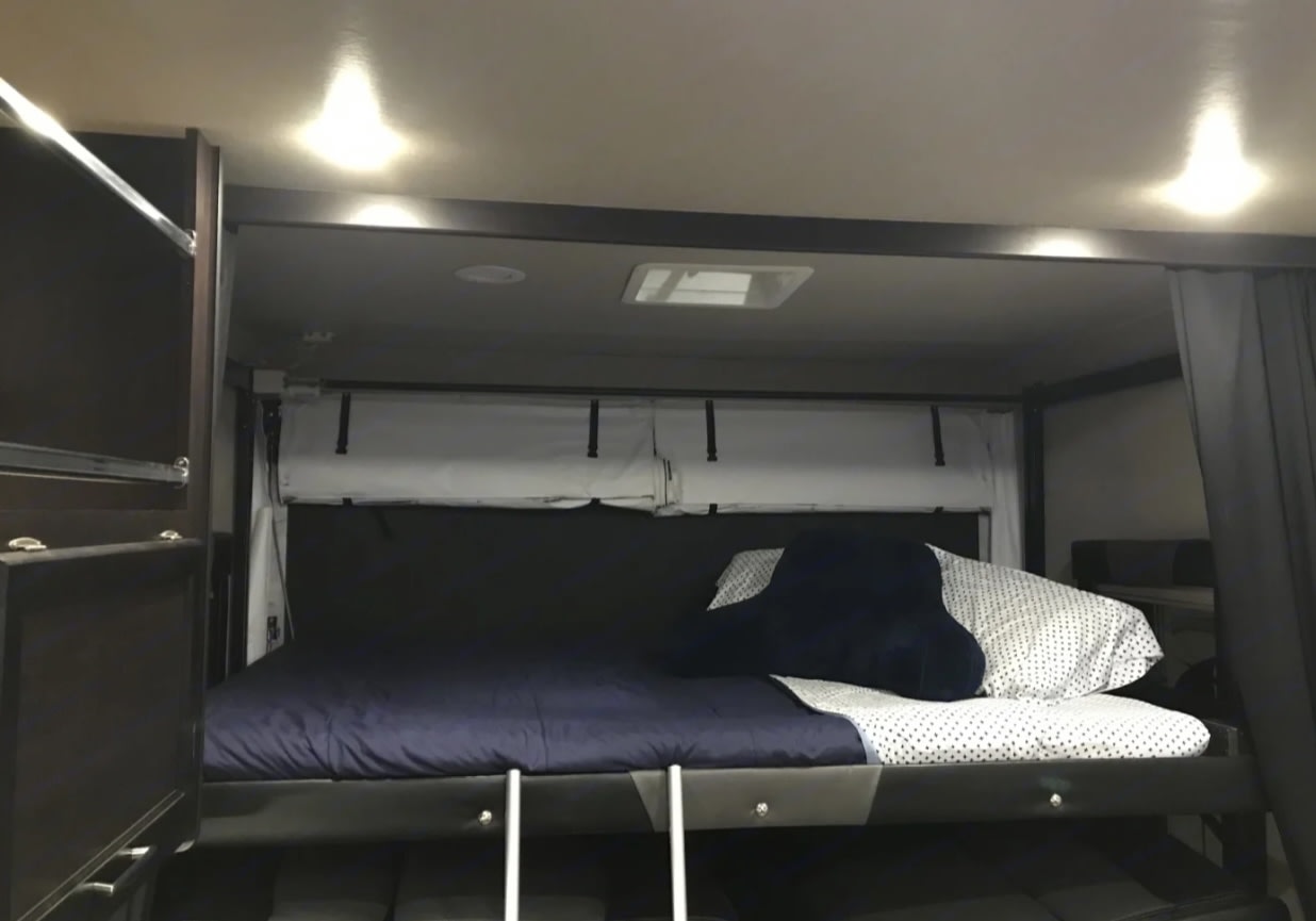 RV rental interior featuring a cozy bunk bed with dark bedding, a ladder, overhead lights, and a ceiling vent.. Alliance RV Valor Toy Hauler 2021