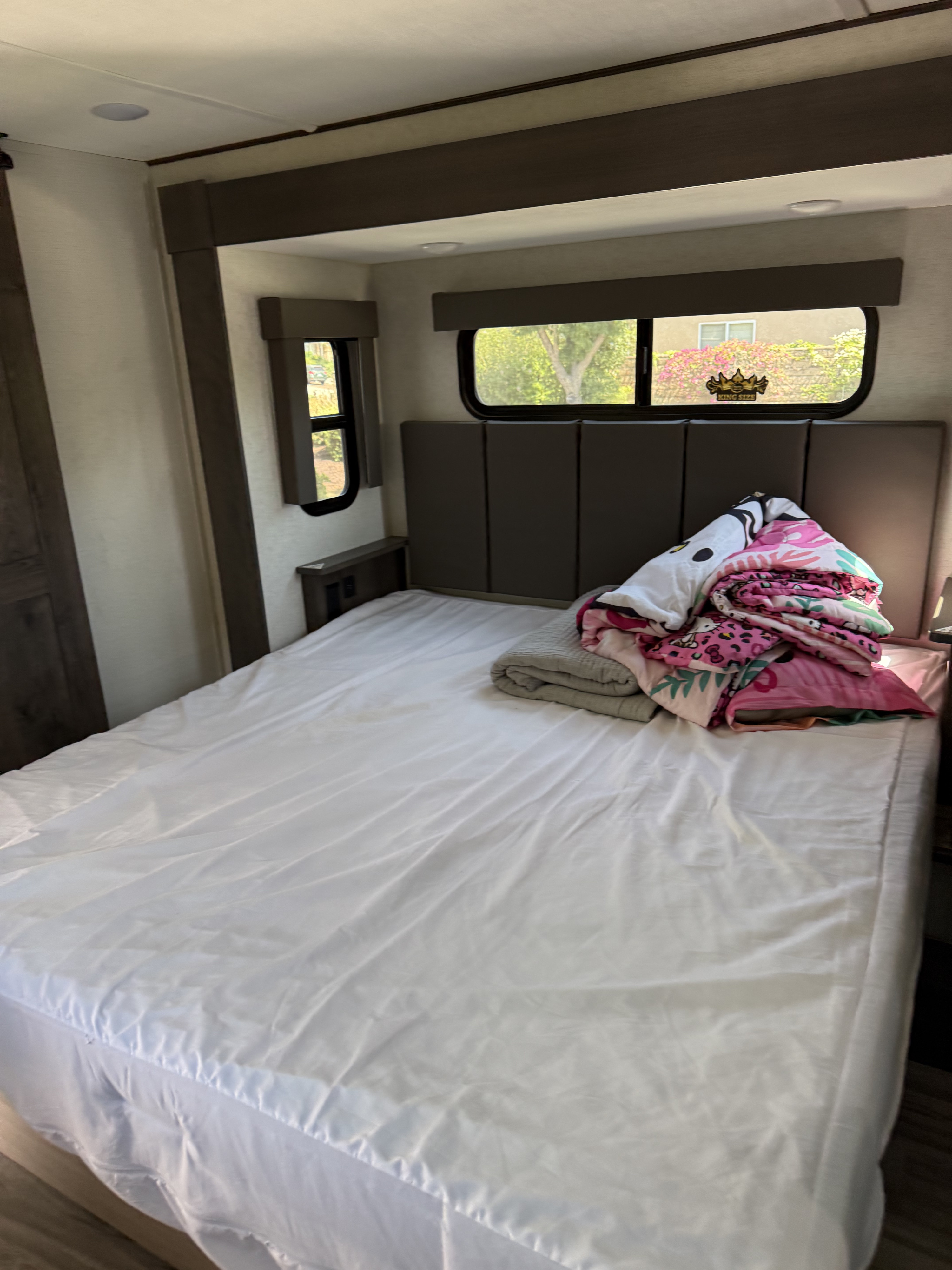 RV rental bedroom interior: a comfortable bed with piled blankets and windows showing outdoor greenery.. Alliance RV Valor Toy Hauler 2021