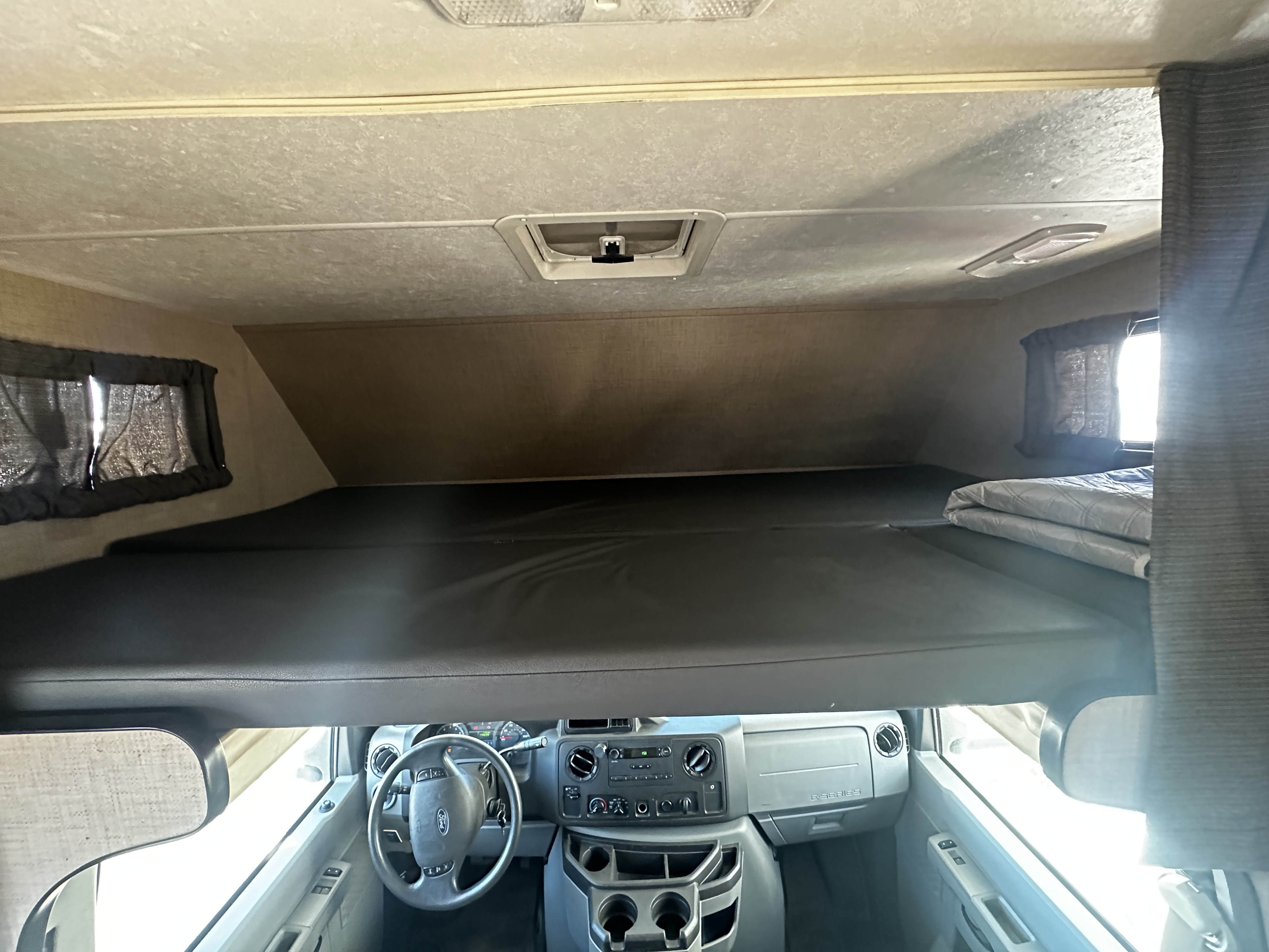 Inside an RV rental: view of the spacious overhead bunk bed over the driver's cabin and dashboard.. Thor Majestic 2019