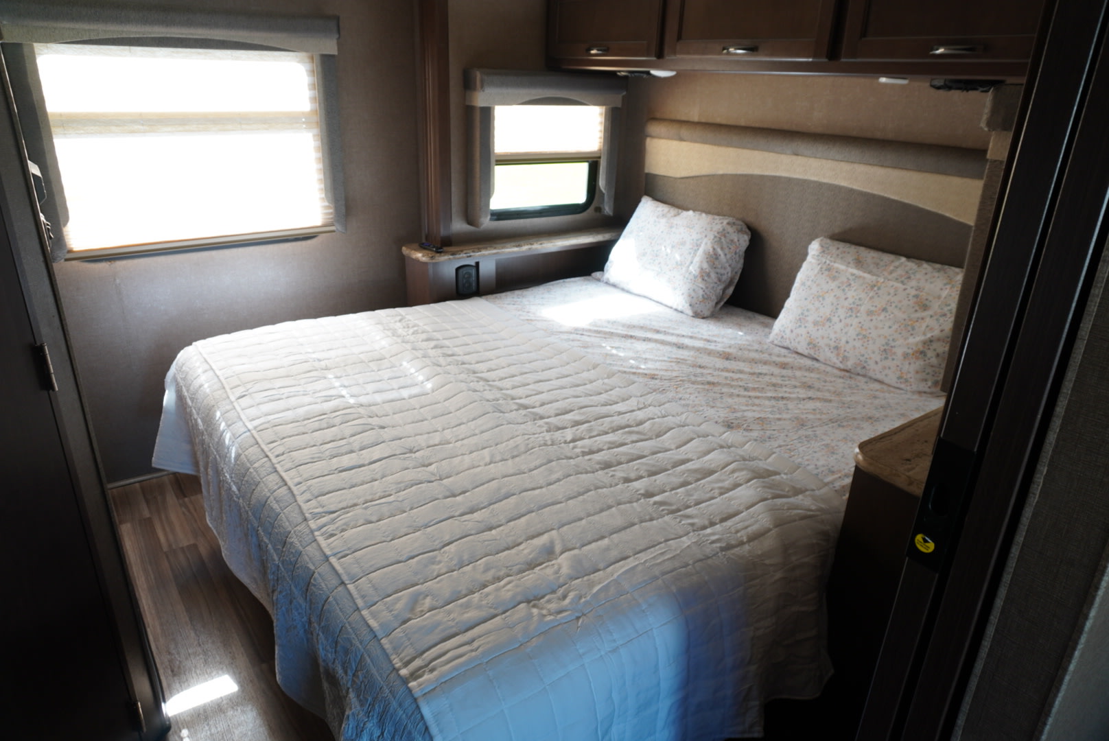 Inside this RV rental: a bright, inviting bedroom featuring a soft bed, windows, and convenient overhead storage.. Thor A.C.E. 2018