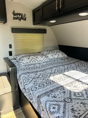 Cozy RV rental bedroom with a patterned bedspread, overhead cabinets, and a "happy campers" sign on the wall.. Forest River Cherokee Wolf Pup 2021