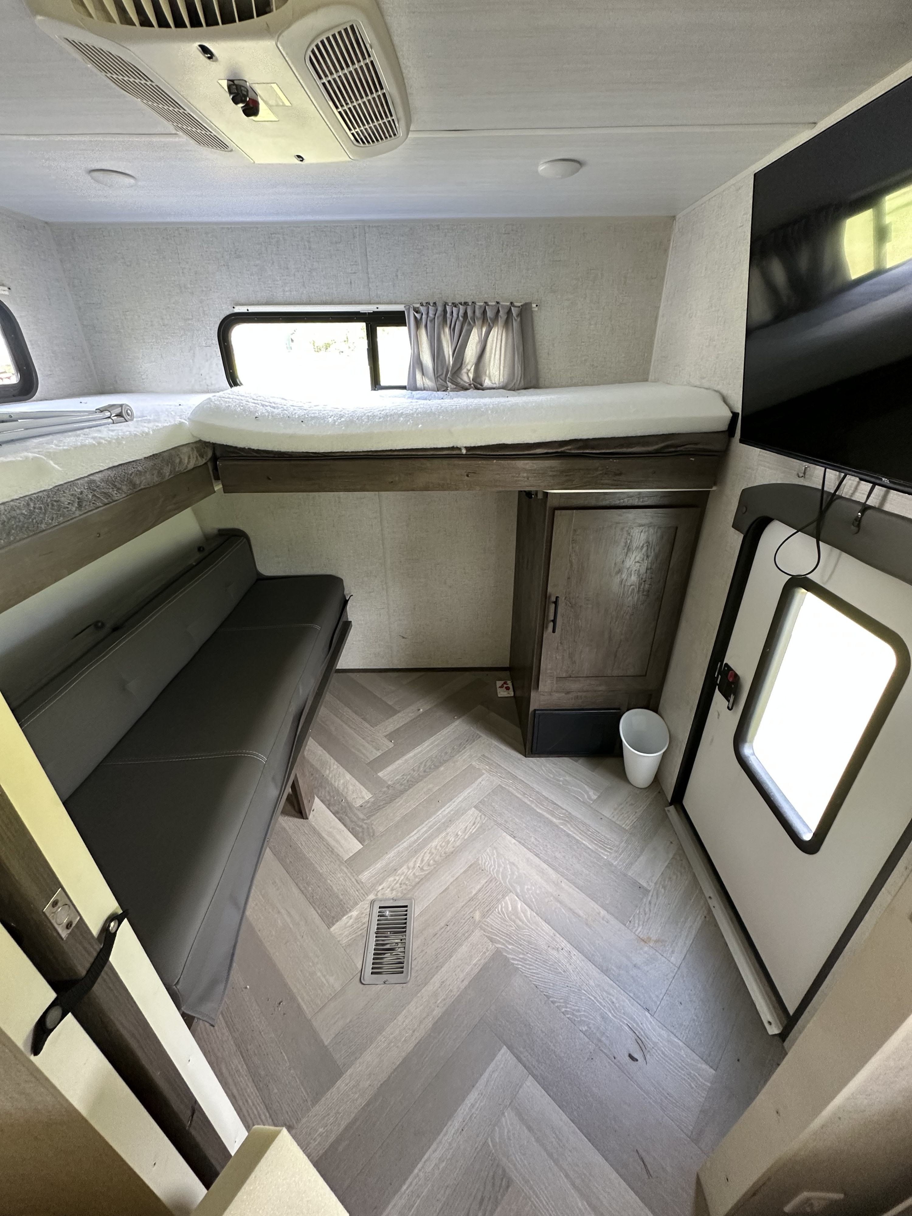 RV rental interior featuring bunk beds, a sofa, herringbone-patterned flooring, and a TV near the entry door.. Forest River Wildwood 2021