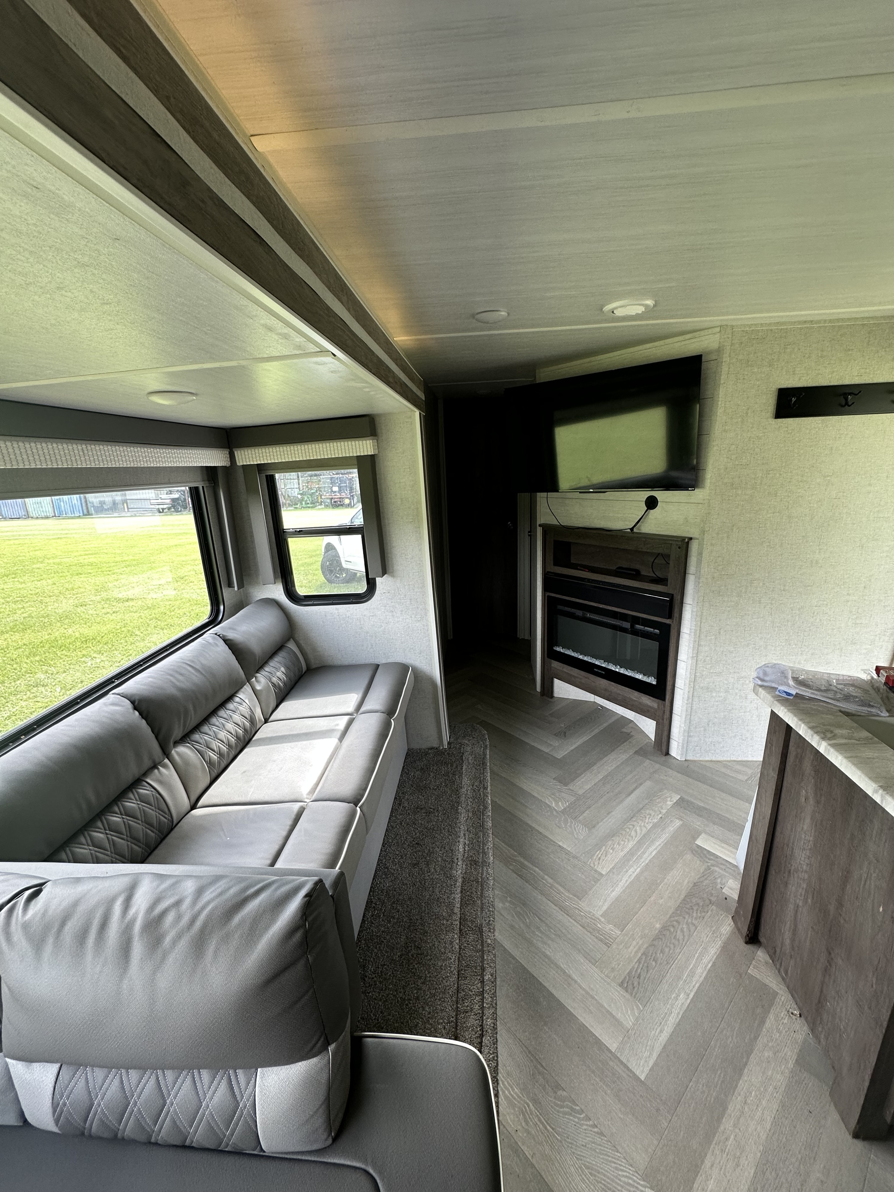 Spacious RV rental living area featuring a grey sofa, TV, electric fireplace, and herringbone flooring. Ideal for comfort.. Forest River Wildwood 2021