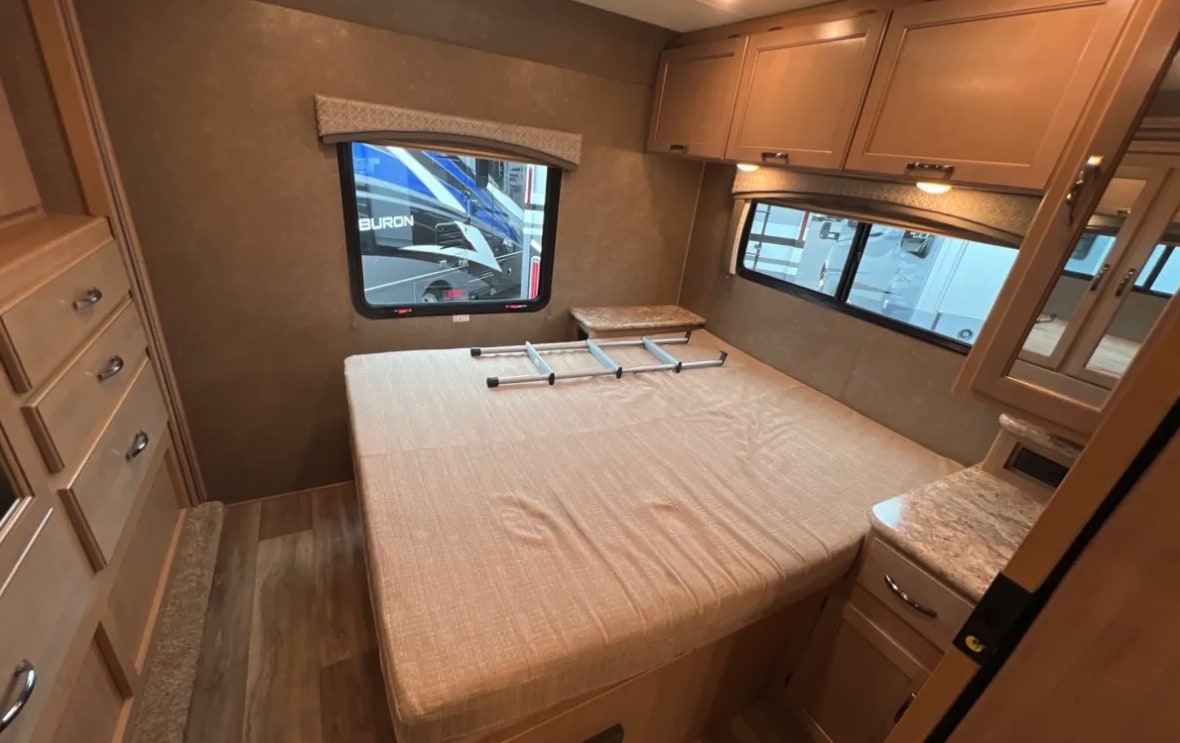 Cozy RV rental bedroom with a comfortable bed, overhead cabinets, a dresser, and windows. A ladder sits on the bed.. Thor Motor Coach 30d 2020