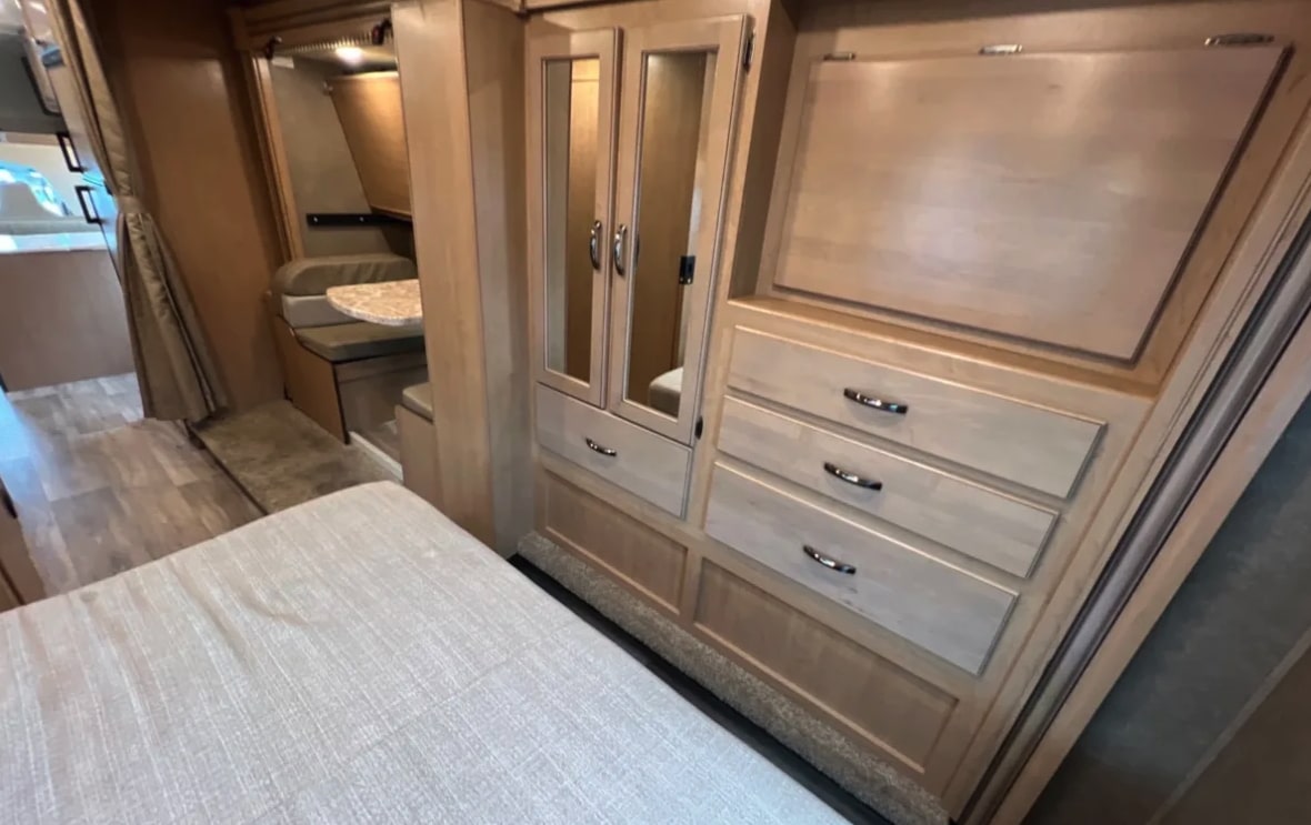 RV rental bedroom area featuring a wardrobe with mirrored doors, drawers, and a dinette in the background.. Thor Motor Coach 30d 2020