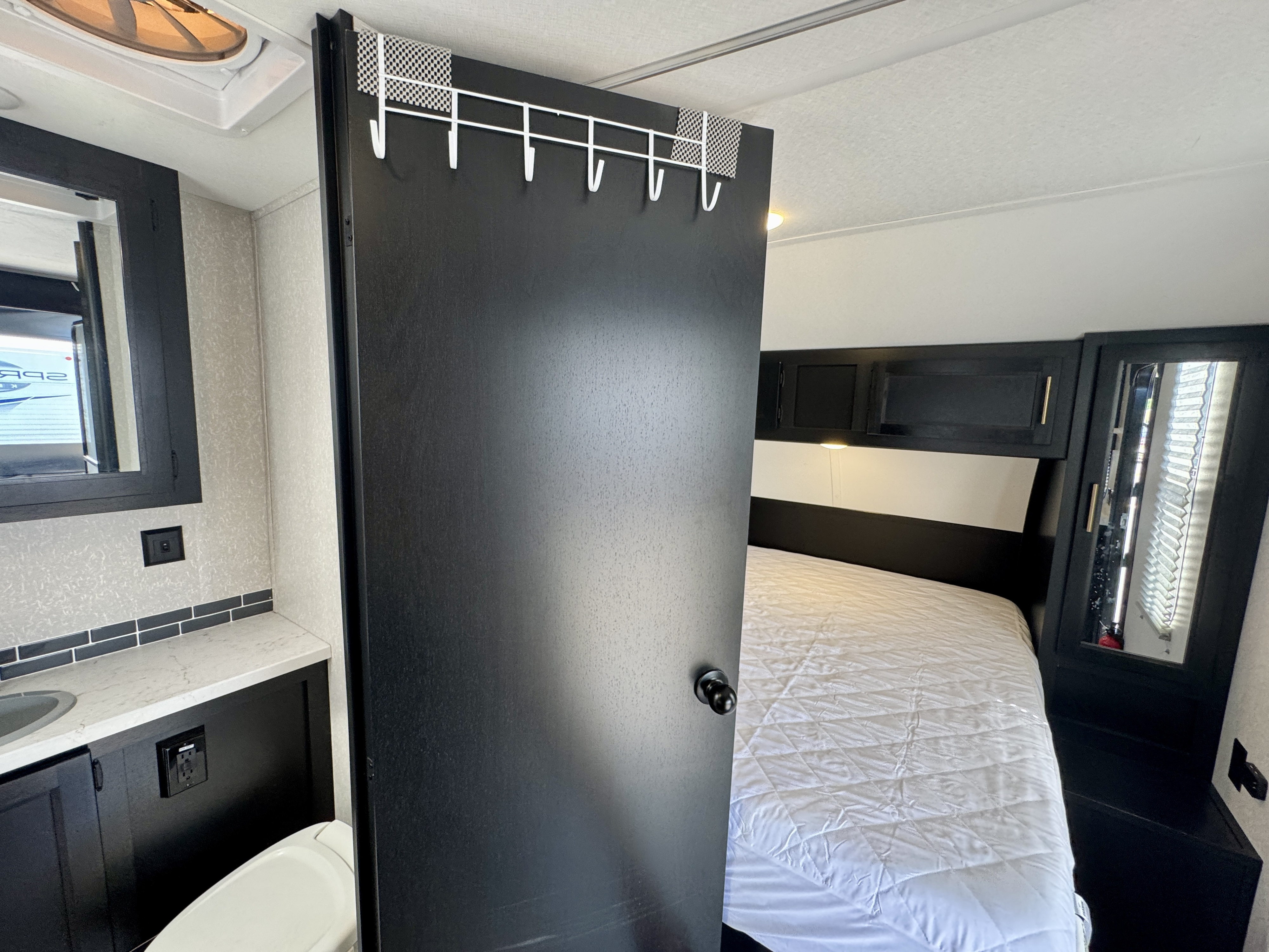 Inside a sleek **rv rental**: a modern bathroom area with vanity & toilet, adjacent to a bedroom with a quilted bed.. Forest River Grey Wolf Limited 2022