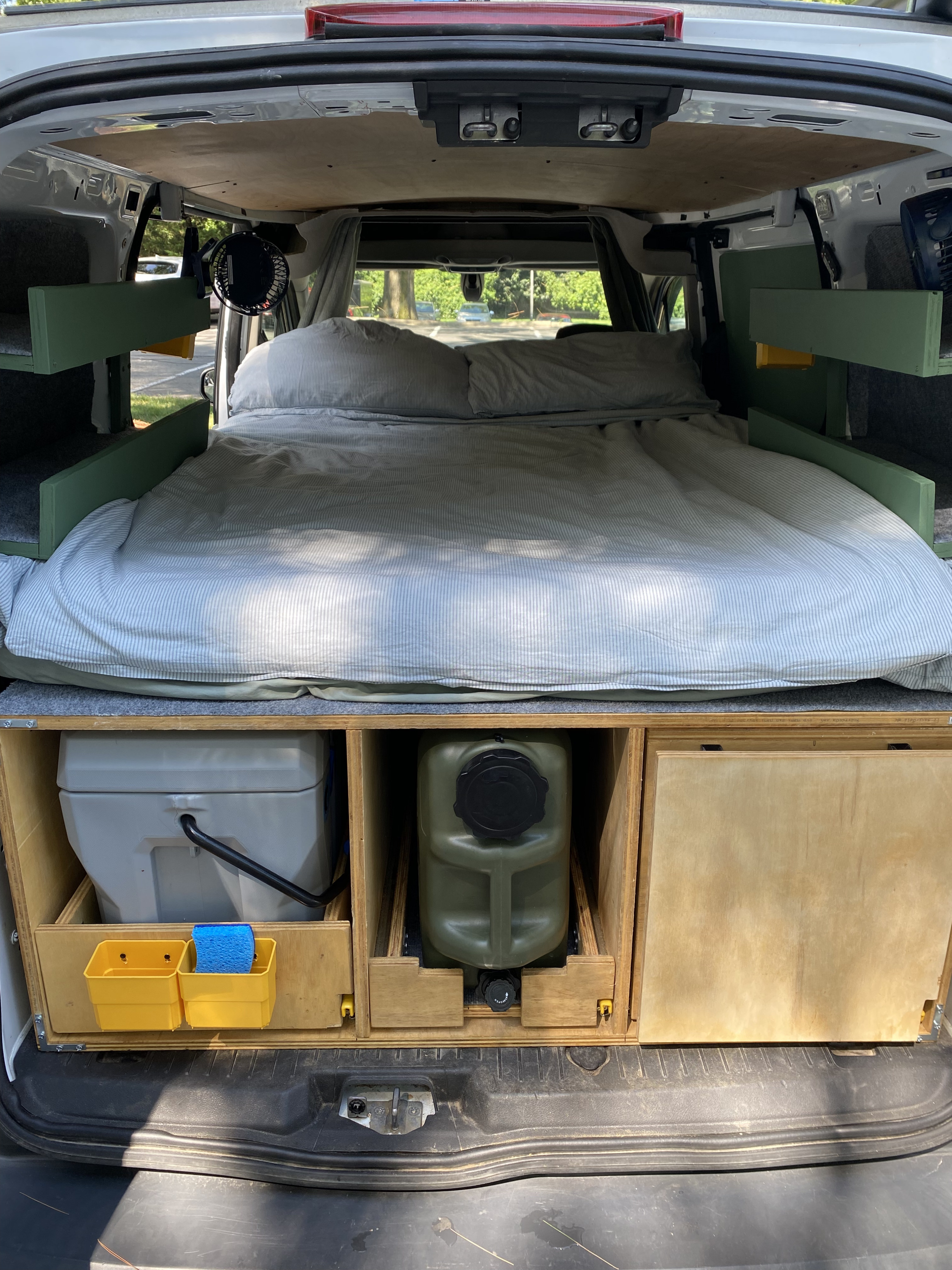 RV rental: Camper van interior with cozy bed, built-in storage for a portable toilet & water, fan, and side shelves.. Ford Custom Transit 2017