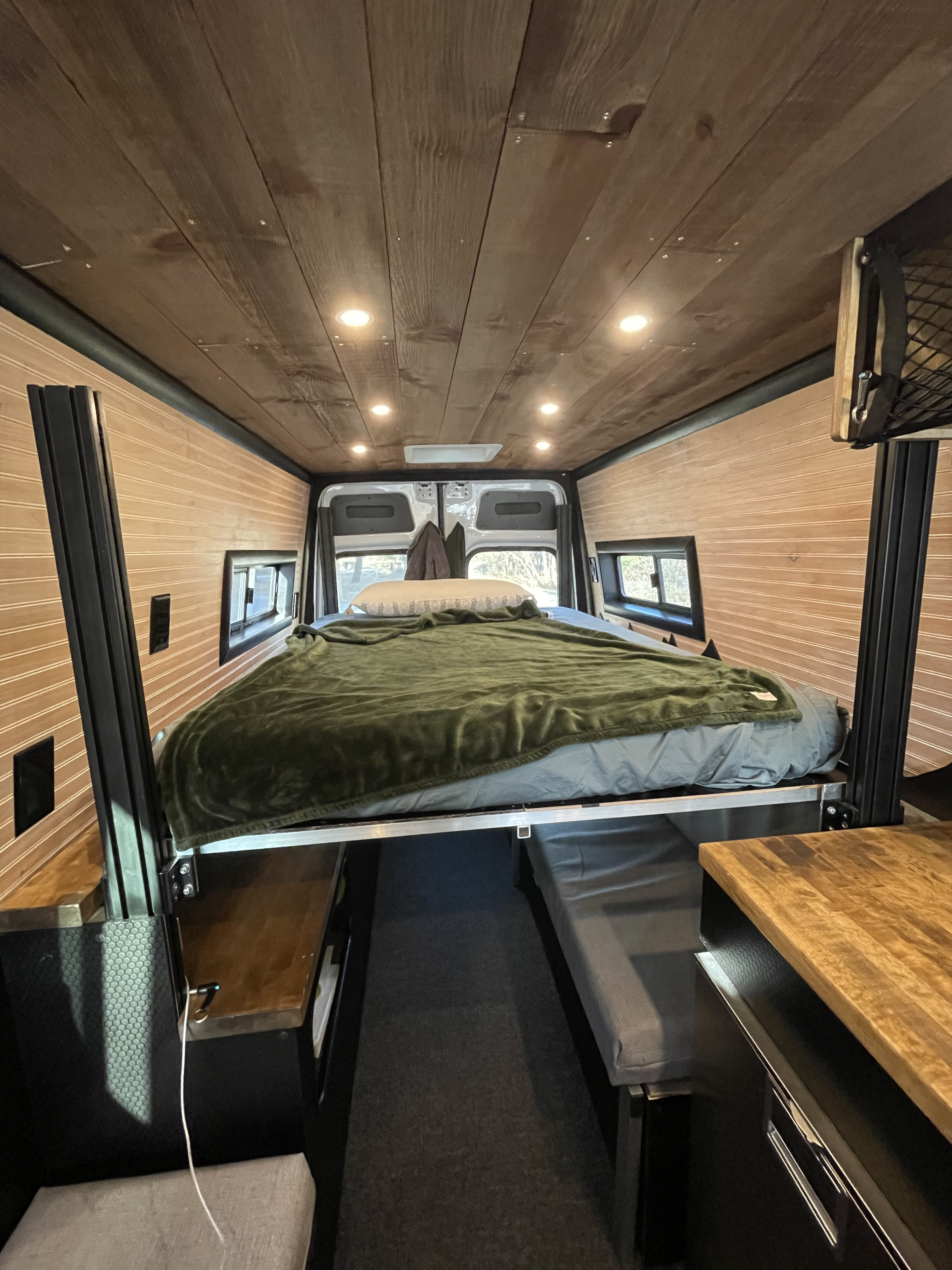 Inside a stylish RV rental, showcasing an elevated bed, wood-clad walls/ceiling, and a functional living space.. Mercedes-Benz Sprinter 3500 2020