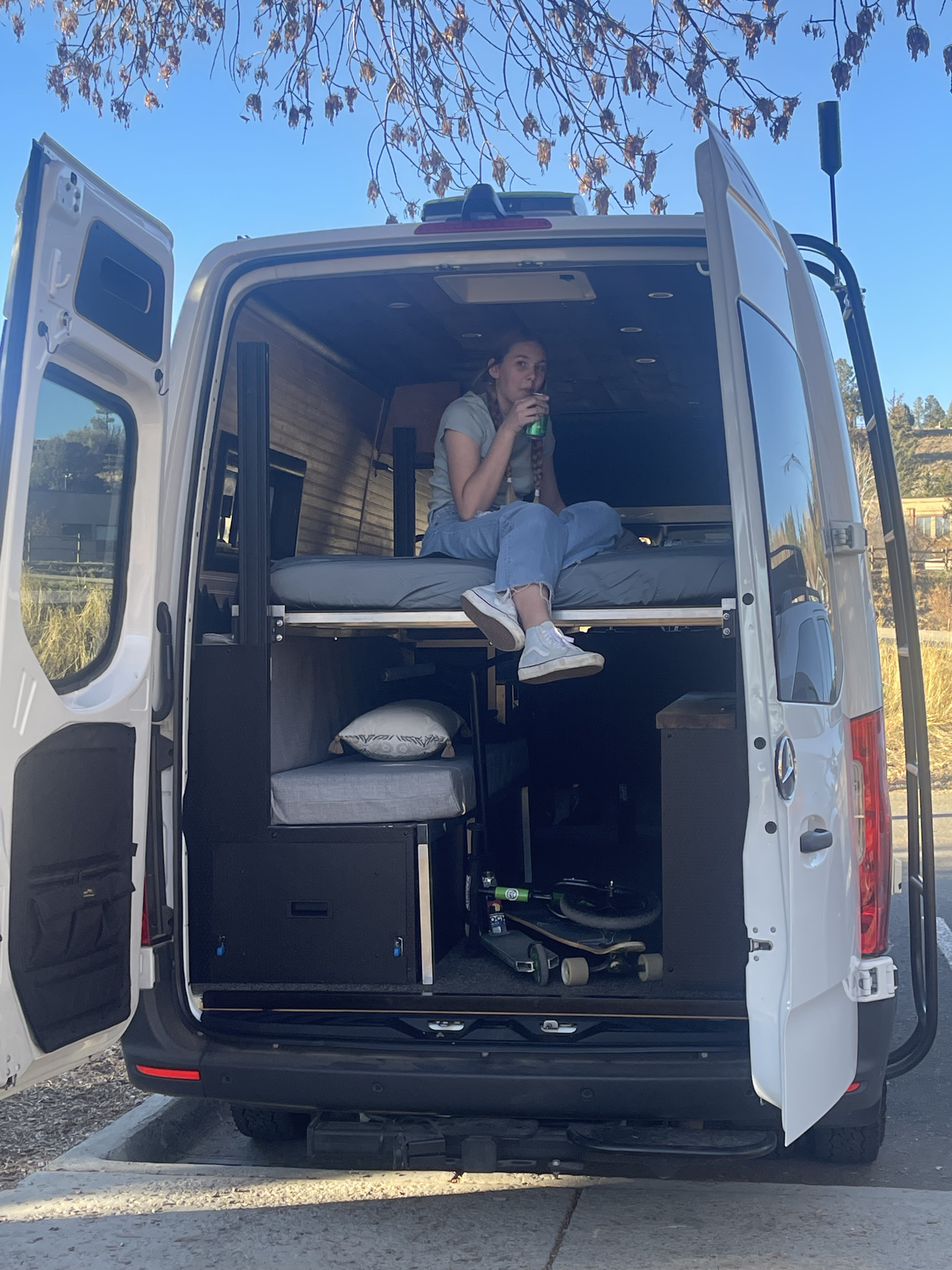 Custom camper van RV rental interior: a woman relaxes on the bed with skateboards stored below.. Mercedes-Benz Sprinter 3500 2020