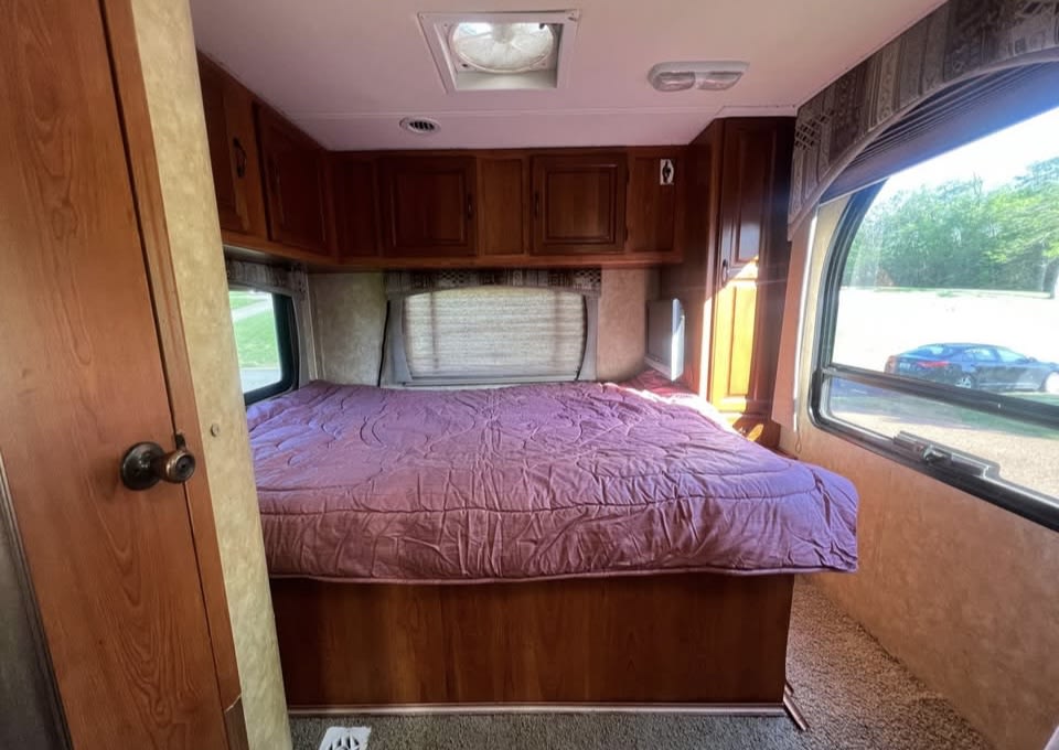 Cozy RV rental bedroom featuring a large purple bed, overhead cabinets, and bright window views of nature.. Coachmen Freedom Express 2009