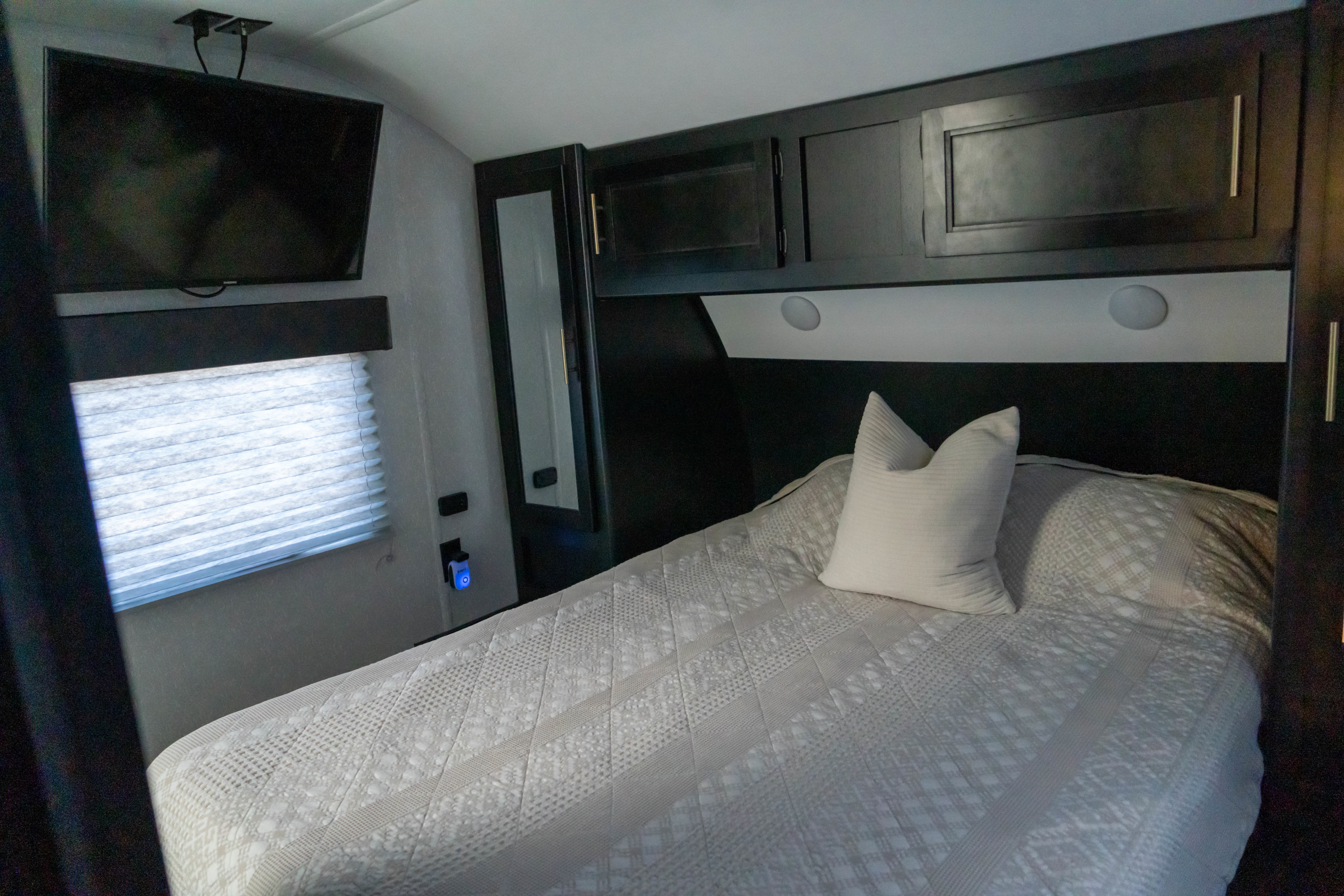 Cozy **RV rental** bedroom with a comfortable bed, wall-mounted TV, dark cabinetry, and window blinds.. Forest River Cherokee 2022