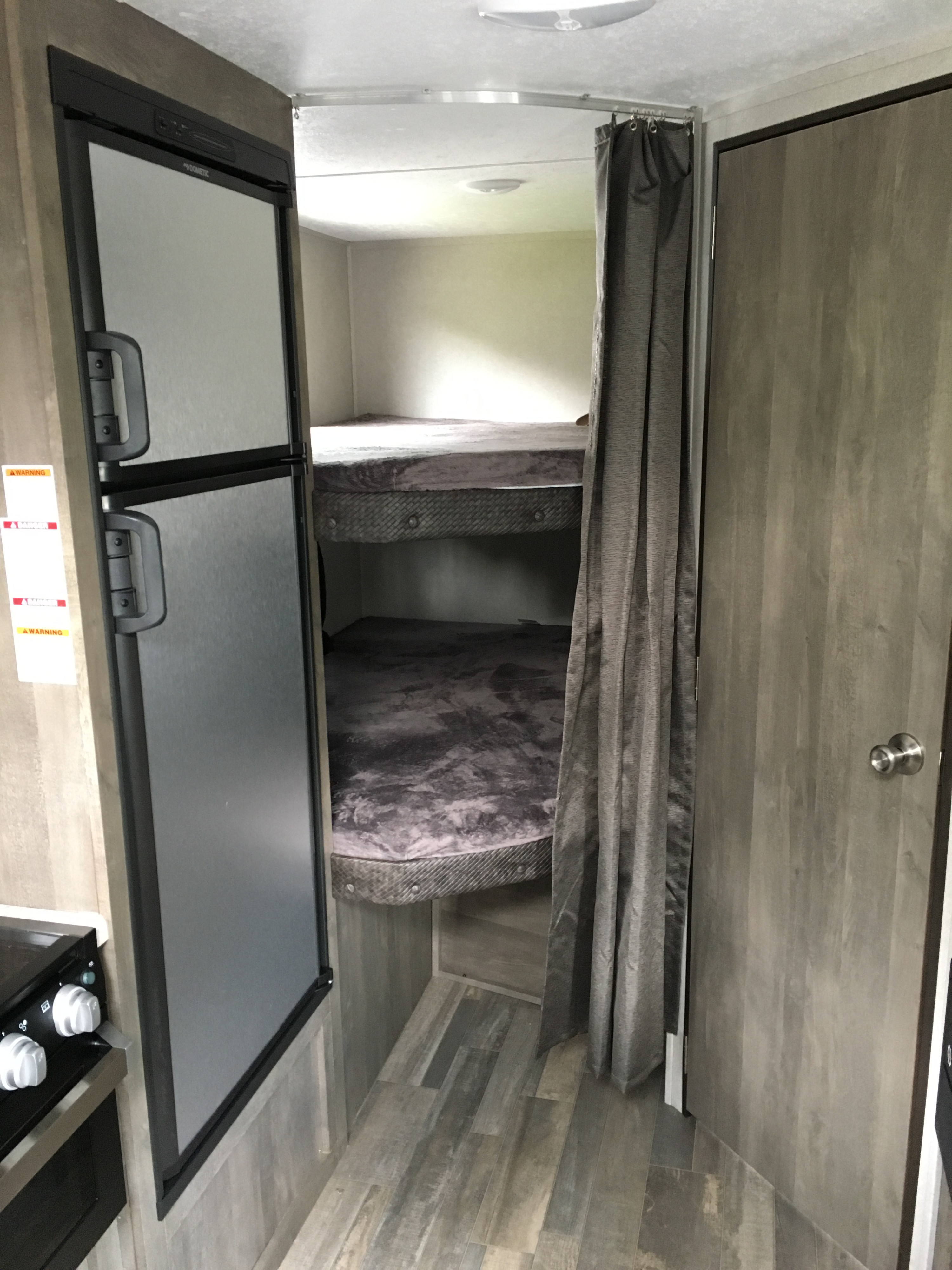RV rental interior: bunk beds with grey bedding, a Dometic fridge, privacy curtain, and wood-look floor in a travel trailer.. Forest River Vibe 2020
