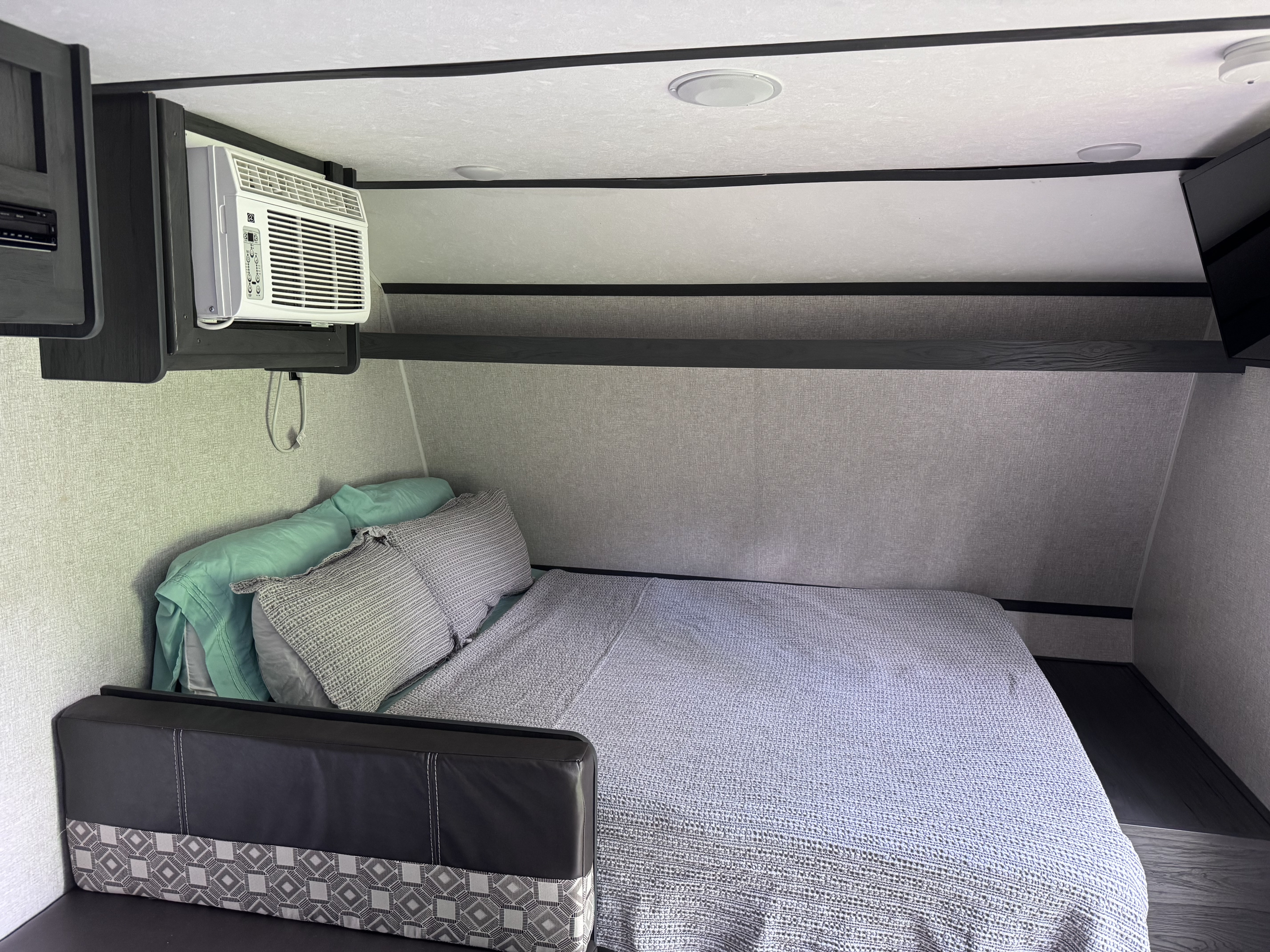 Bright RV rental bedroom: bed with grey/teal bedding, overhead AC unit, and corner bench.. Dutchmen Other 2021