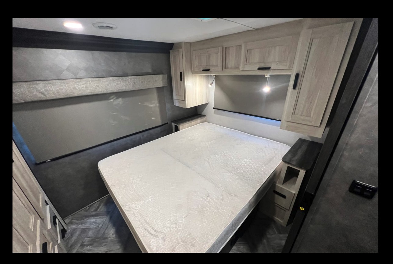 Modern RV rental bedroom with a large, clean mattress, overhead cabinets, and window blinds for a comfortable stay.. Forest River Sunseeker 2021