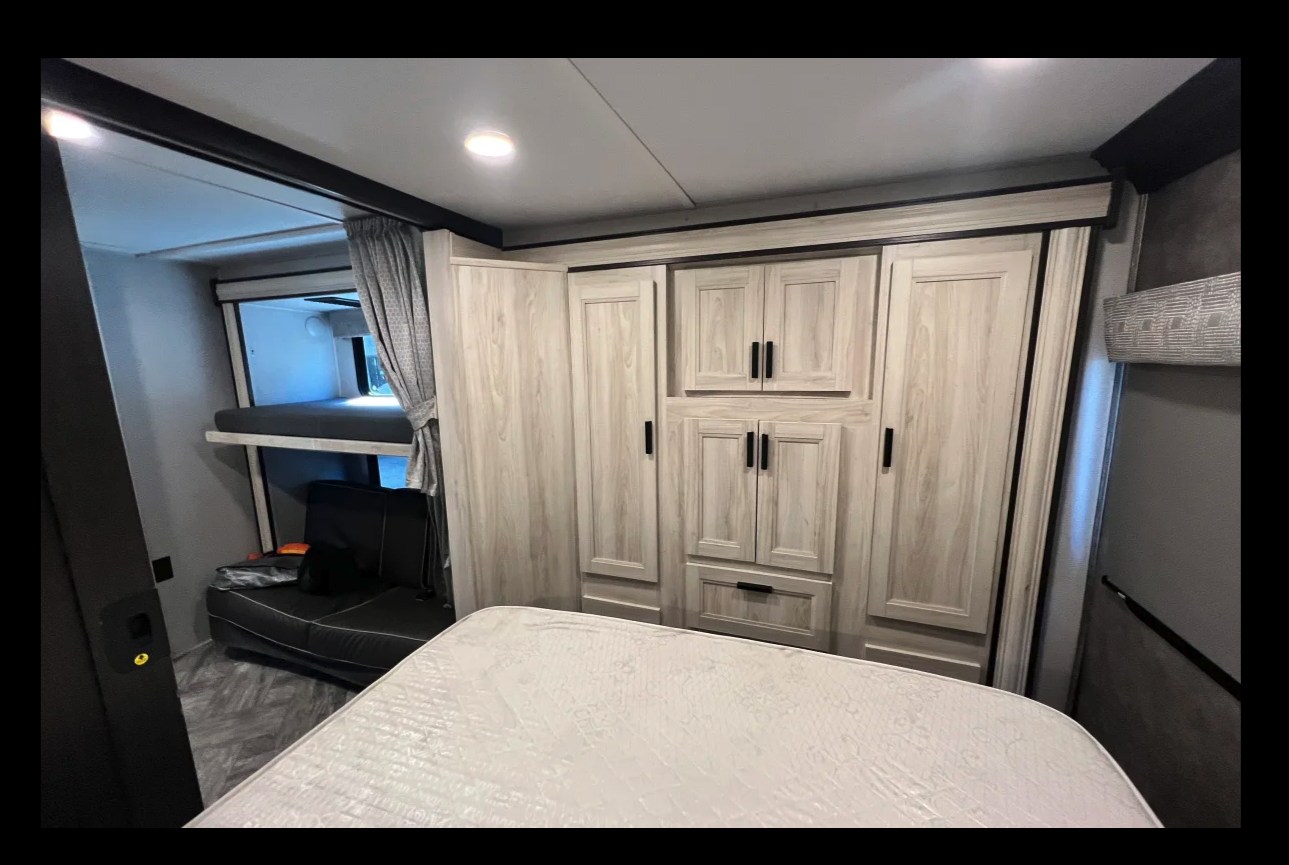 Explore this cozy RV rental bedroom, featuring a main bed, bunk beds, and ample storage cabinets.. Forest River Sunseeker 2022