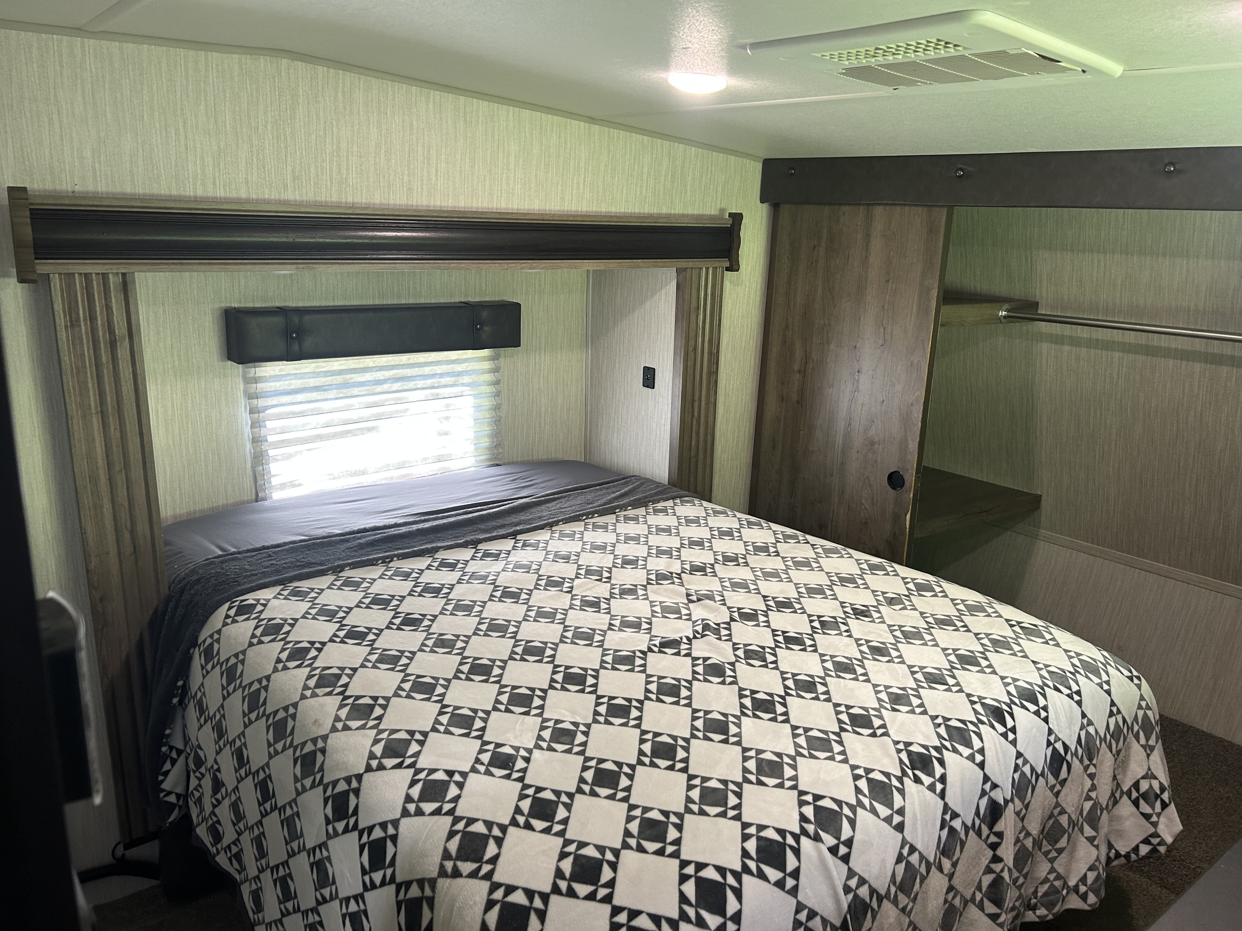 Inside an RV rental, a bedroom showcasing a bed with a geometric blanket, window, and wood-paneled closet.. Forest River Vengeance 2020