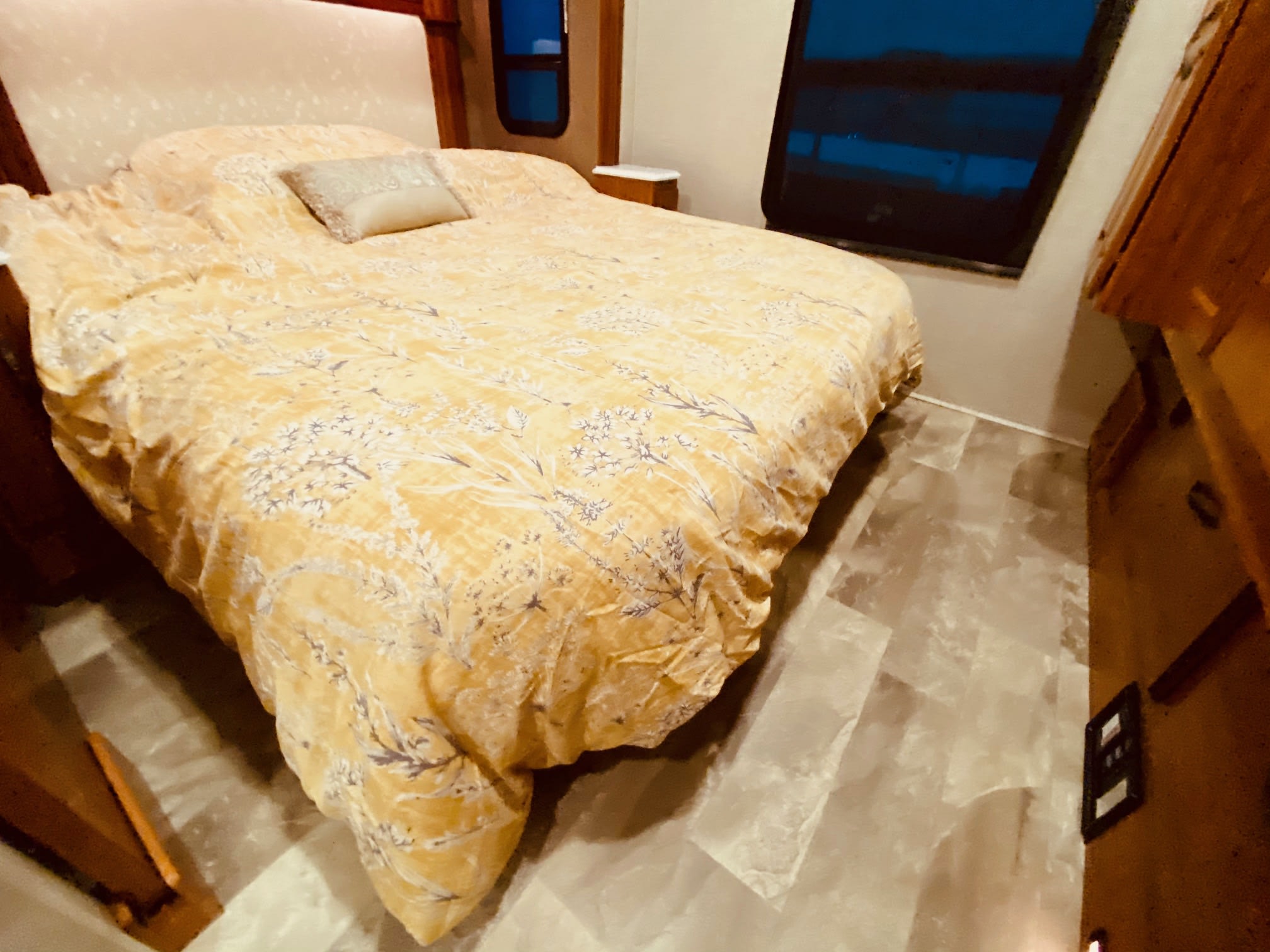 Cozy RV rental bedroom with a comfortable bed, floral comforter, and window, ready for a restful journey.. Jayco Seneca 2018