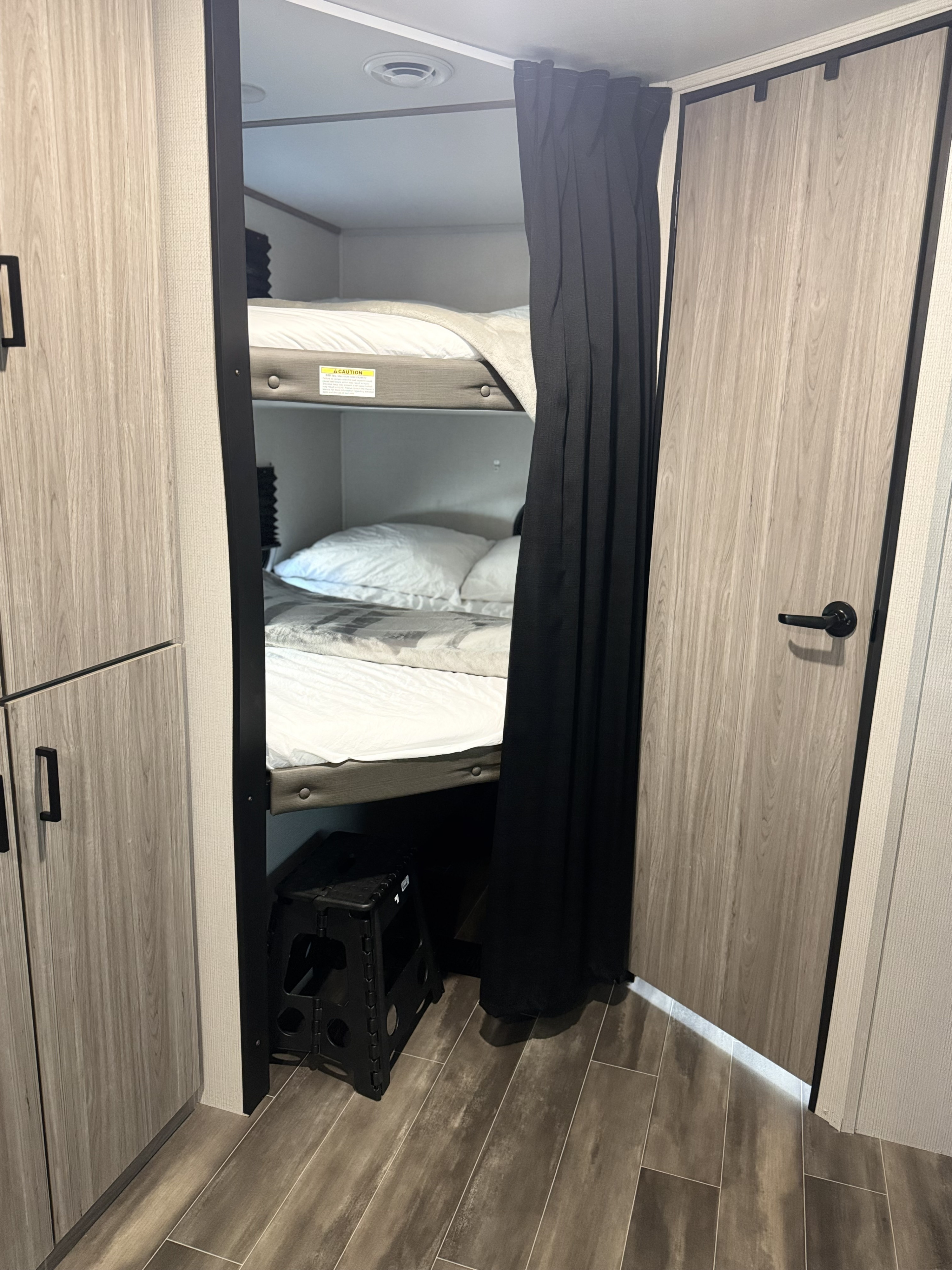 Inside an RV rental: two compact bunk beds with privacy curtain, a step stool, and wood-look cabinetry for storage.. Keystone RV Passport TT 2022