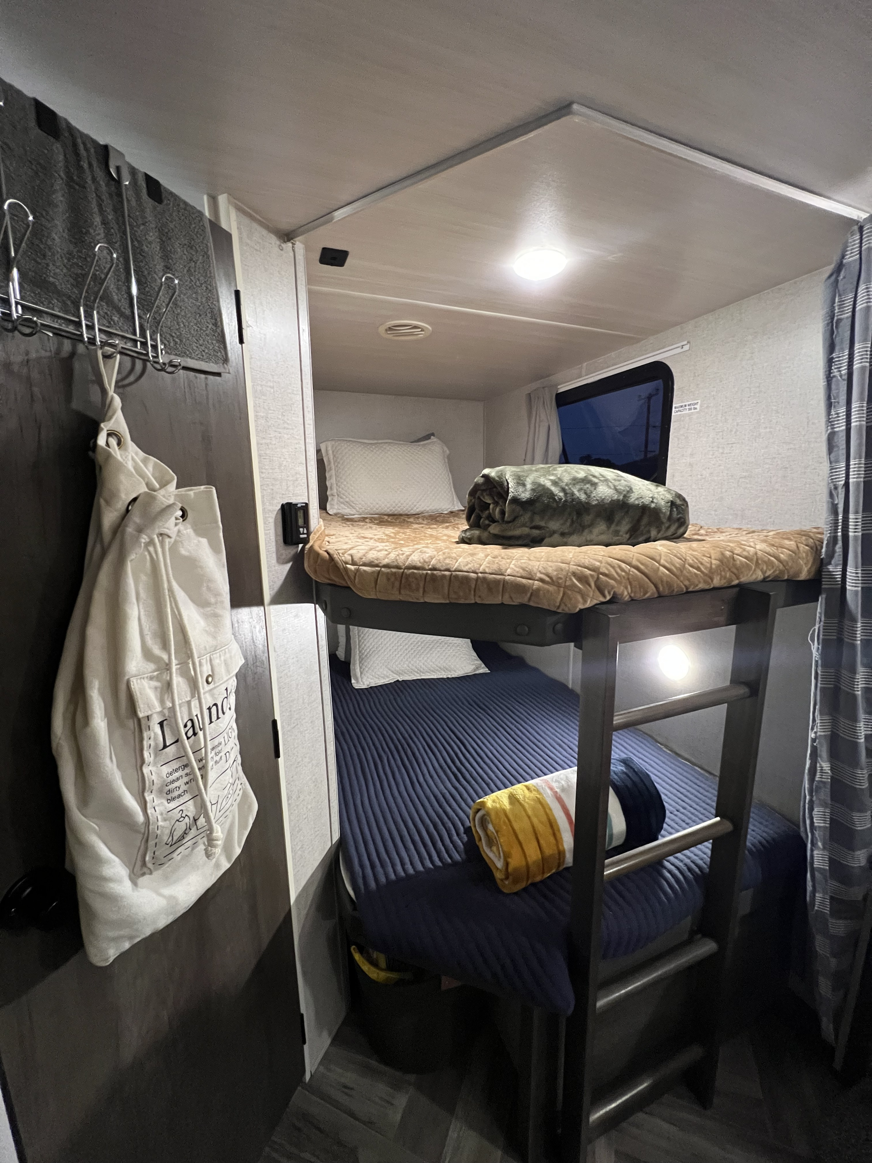 An RV rental's cozy interior, showcasing compact bunk beds with a ladder and comfortable bedding.. Forest River Wildwood X-Lite 2022