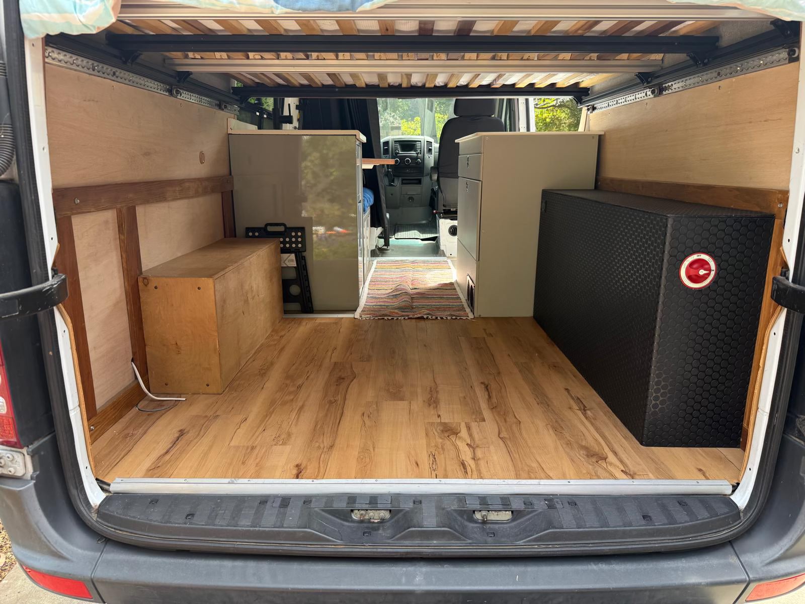 Van conversion RV rental: rear view of organized interior with wooden floor, built-in cabinetry, storage, and bed frame.. Mercedes-Benz Sprinter 2014