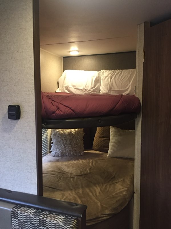 Cozy RV rental interior with bunk beds. The top bunk features red bedding, the lower one has brown bedding and plush pillows.. Heartland RVs Prowler Lynx 2016