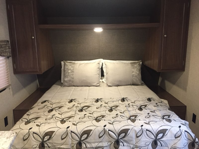 RV rental bedroom: cozy queen bed, decorative comforter, pillows, overhead cabinets, and a reading light, with side shelves.. Heartland RVs Prowler Lynx 2016