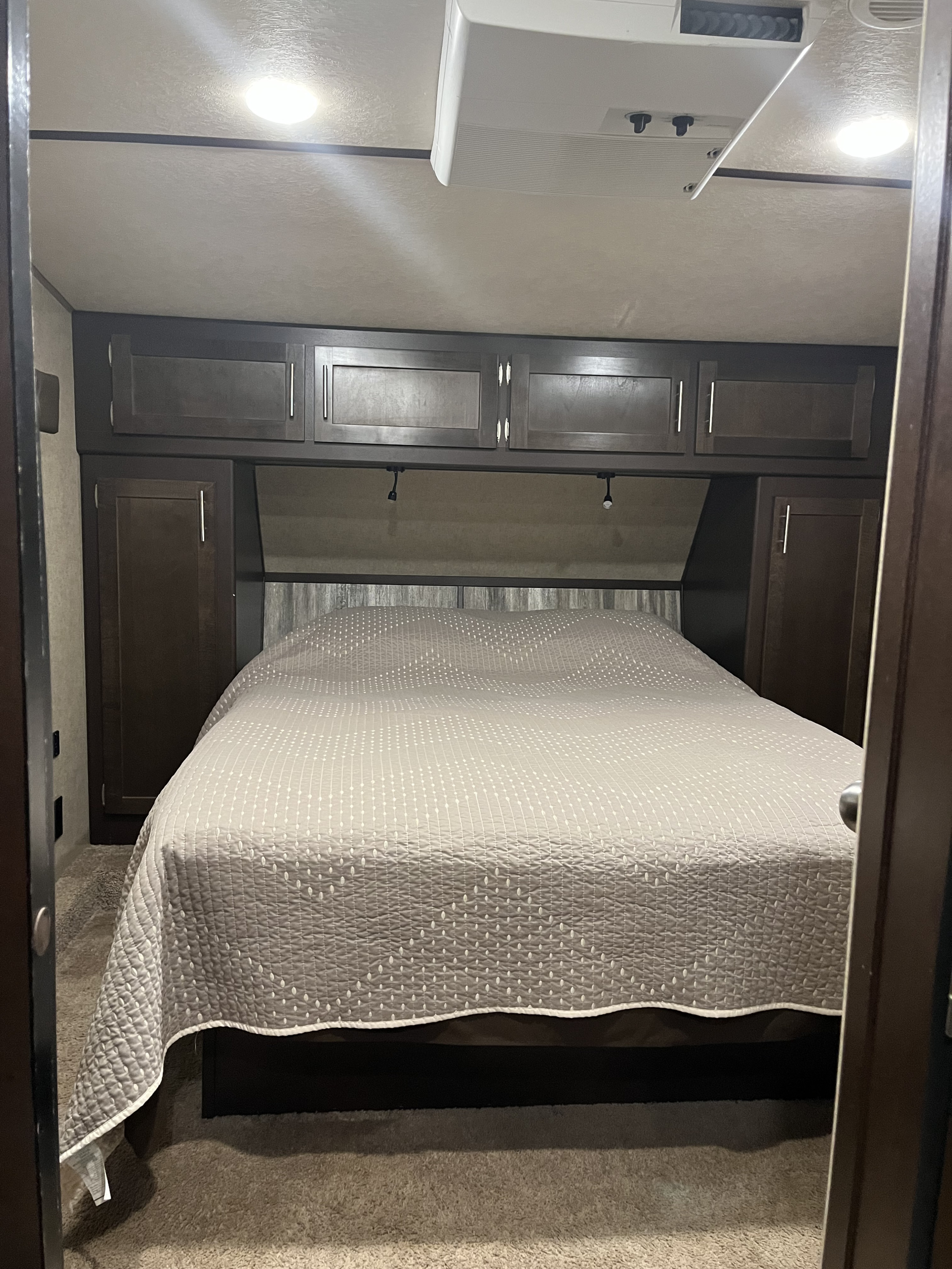 Cozy RV rental bedroom featuring a comfortable bed with patterned quilt, overhead storage, and integrated lighting.. Forest River Wolf Pack 2018