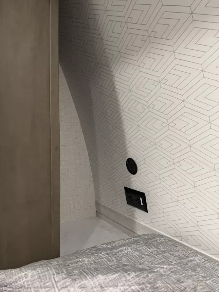 Compact RV rental bedroom with modern geometric wallpaper, convenient power outlets, and a cozy bed.. Grand Design Transcend One 2025