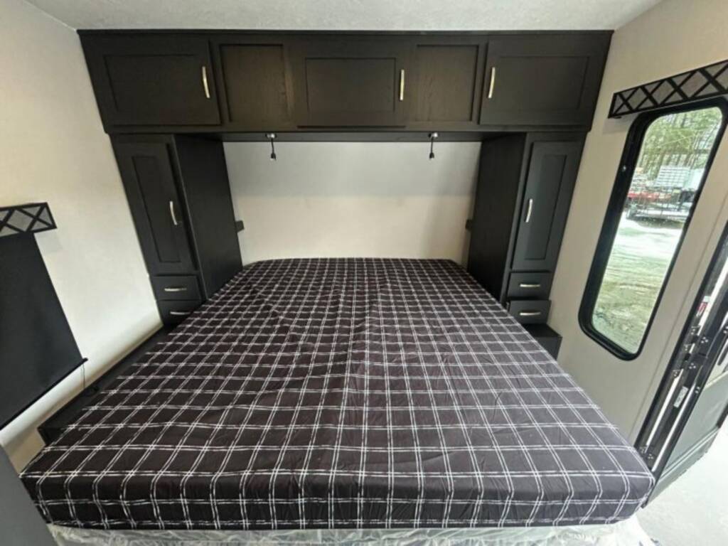 Spacious RV rental bedroom with dark cabinets, a cozy plaid bed, and ample storage for travel comfort.. Forest River Rockwood High Wall 2023