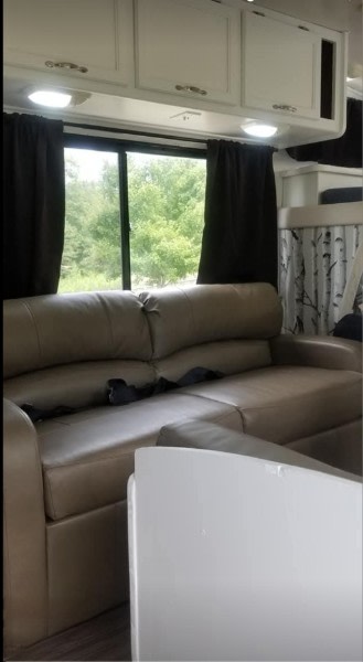 Inside a comfortable RV rental: tan leather sofa, white overhead cabinets, and large window overlooking trees.. Coachmen Leprechaun 2001