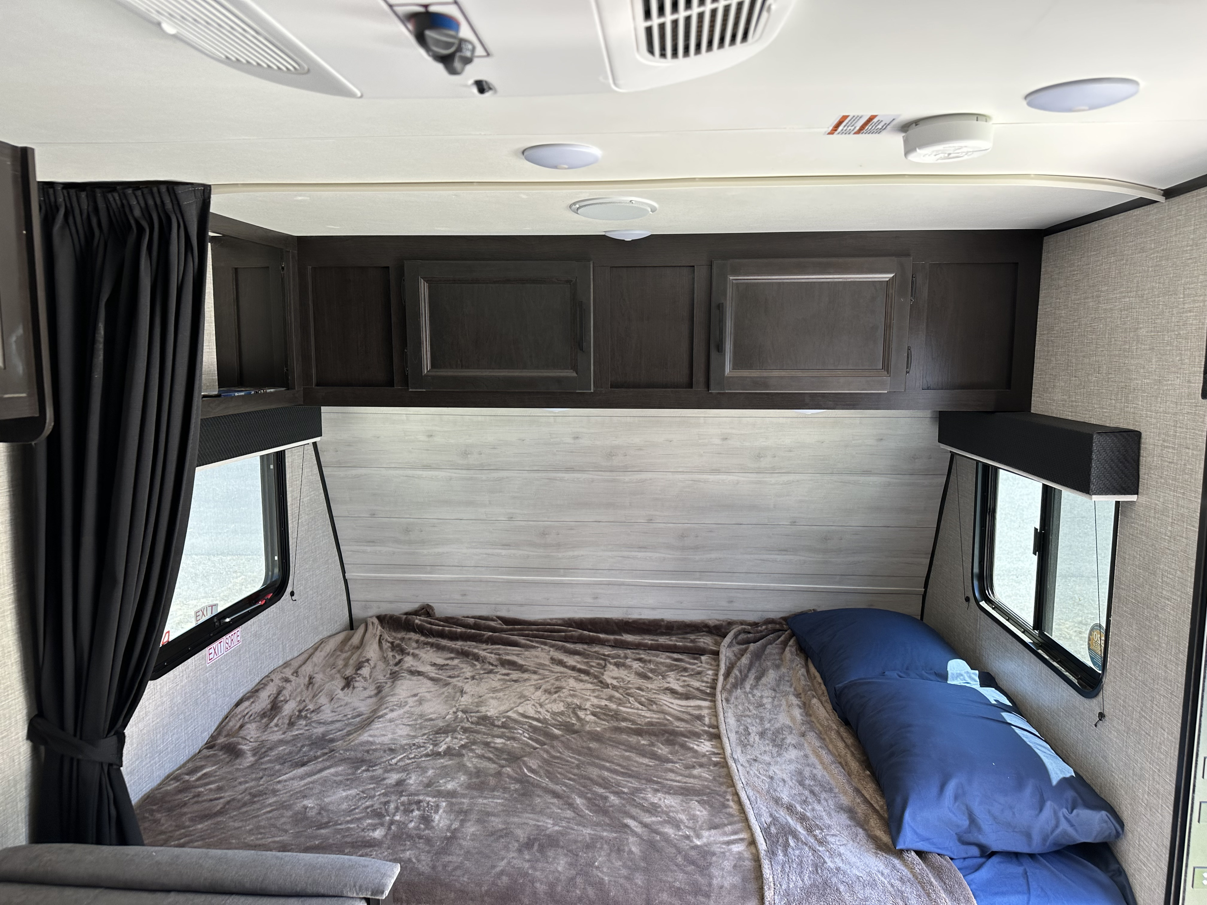 RV rental interior showing a small bedroom with a bed, dark cabinets, two side windows, and a cozy blanket.. Jayco Jay Flight SLX Baja Edition 2021