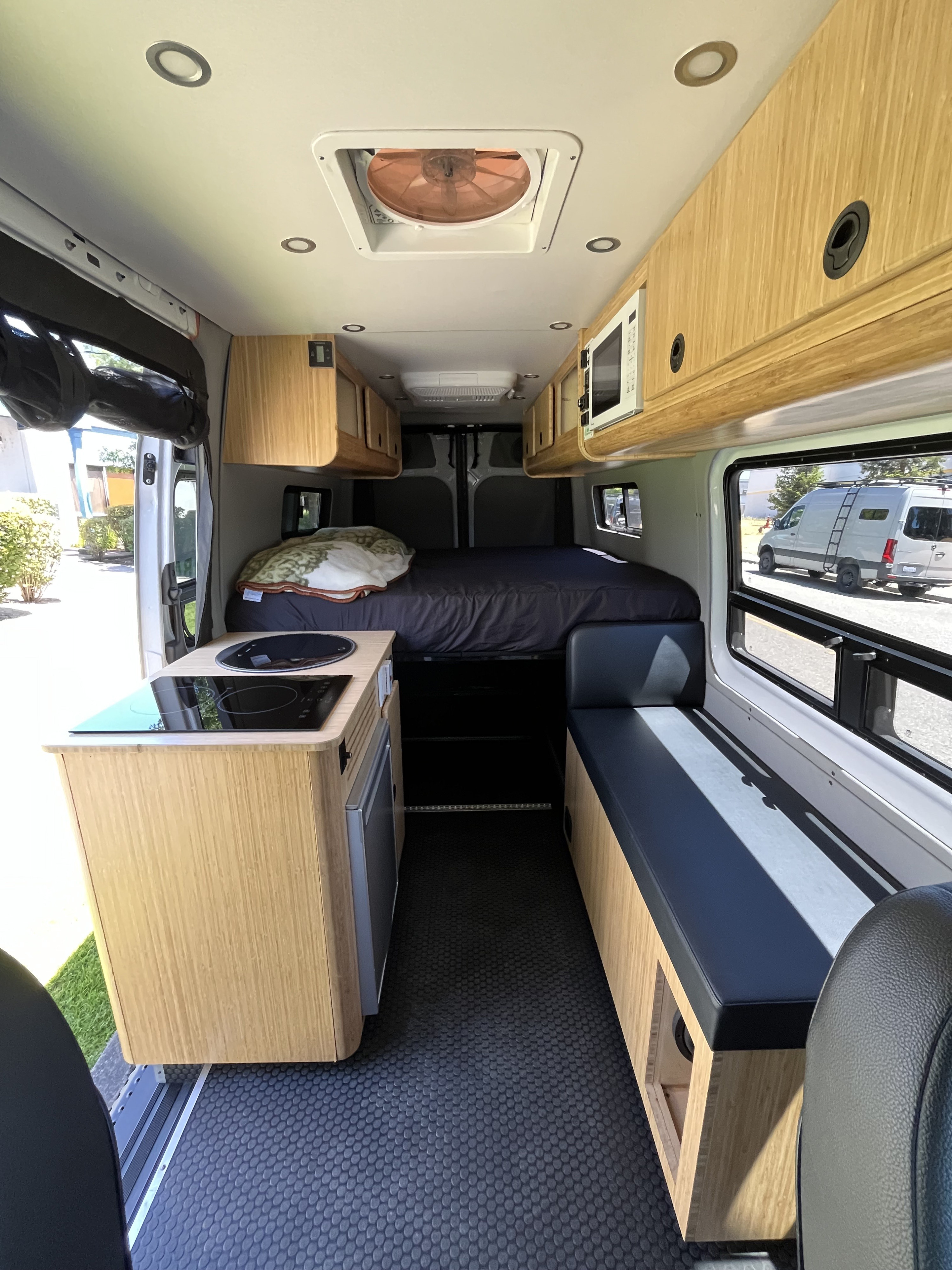 Bright RV rental interior features a kitchen, cozy bed, bench seating, and wood cabinets for comfortable travel.. Mercedes Sprinter Sprinter 2500 2021