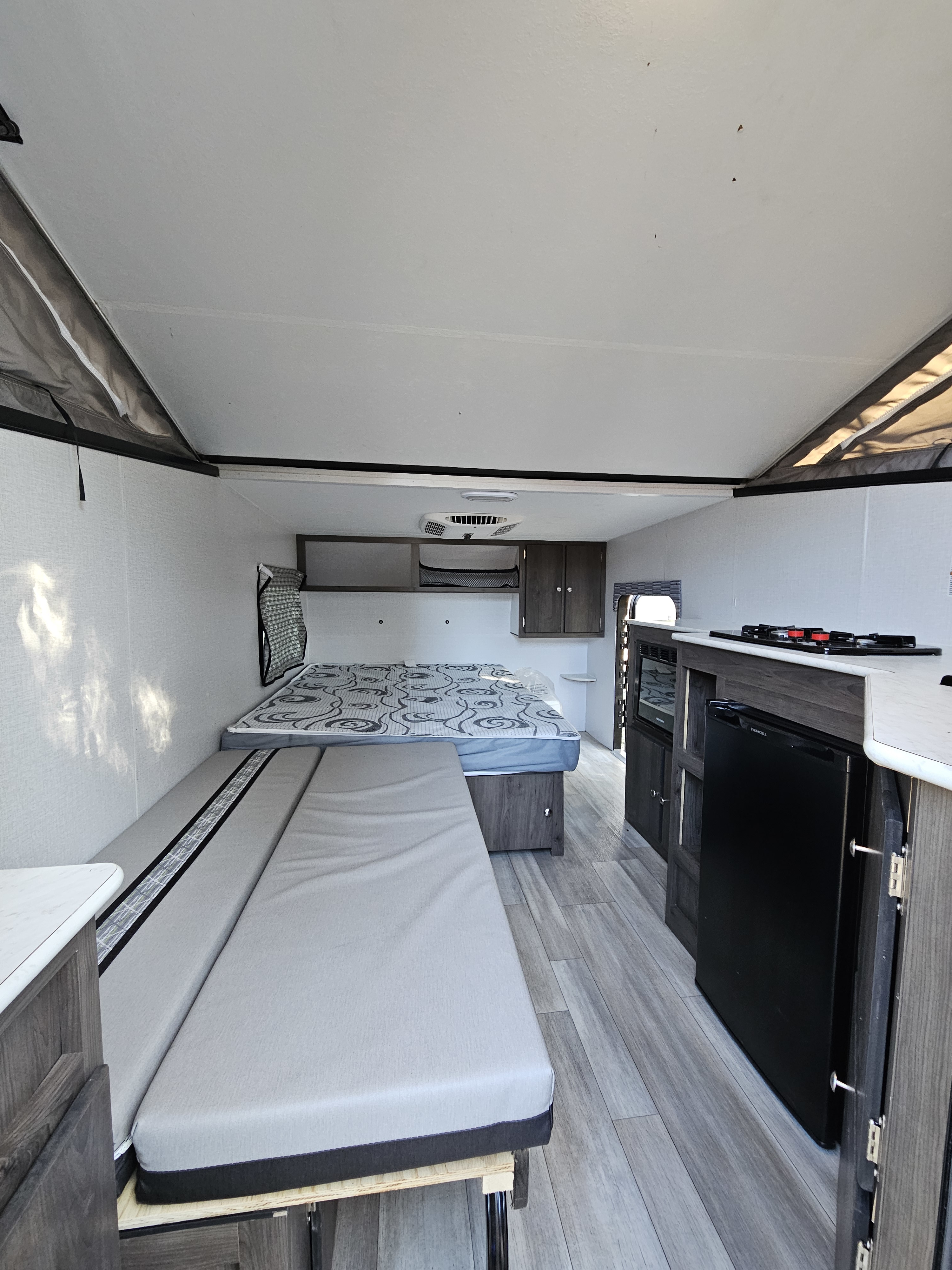Bright RV rental interior: features a bed, bench, and kitchen in a spacious pop-up camper layout.. Forest River V-Cross 2022