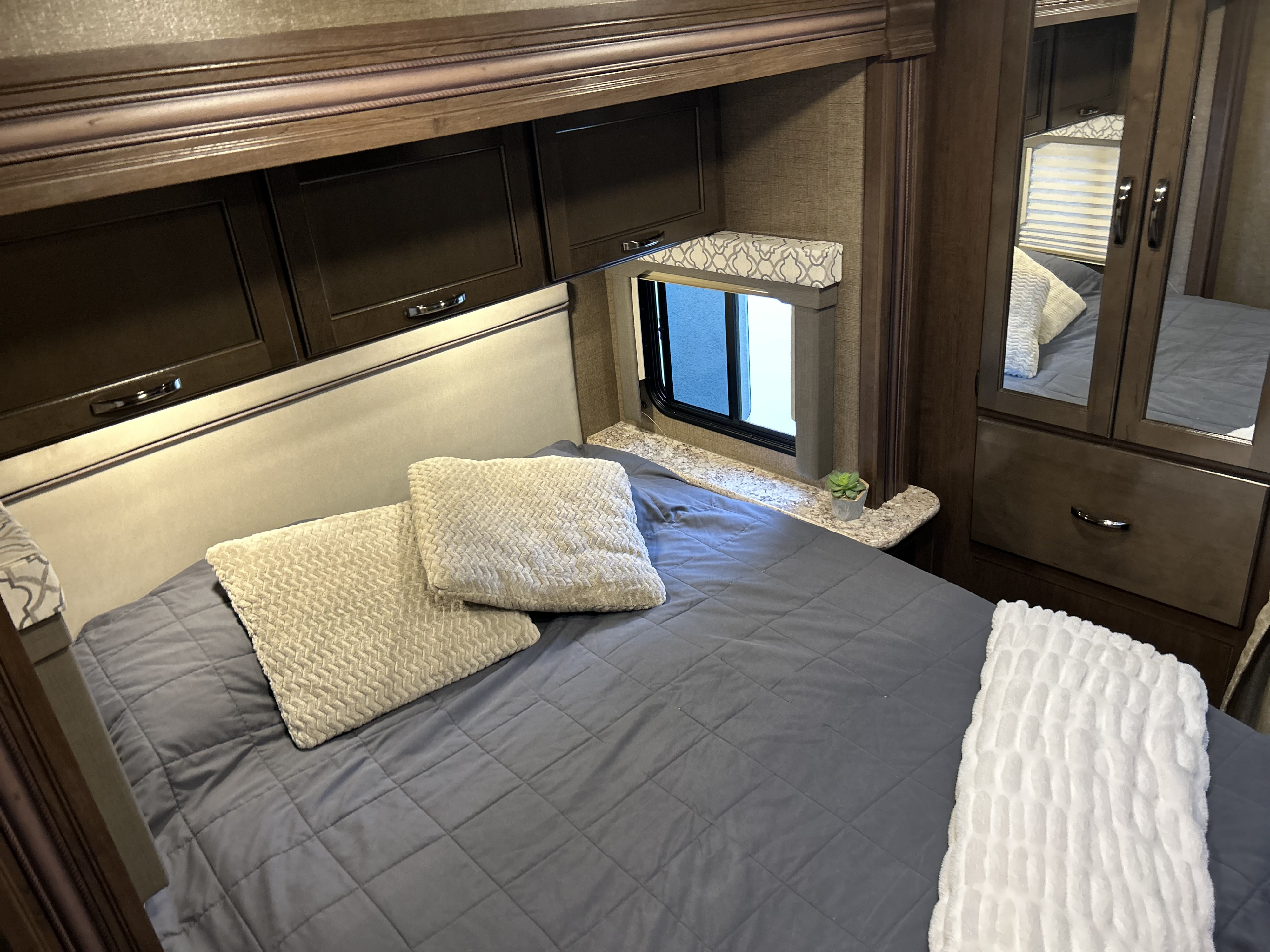 Cozy RV rental bedroom featuring a comfy bed, dark overhead cabinets, a side window, and a mirrored closet.. Thor Freedom Elite 2019