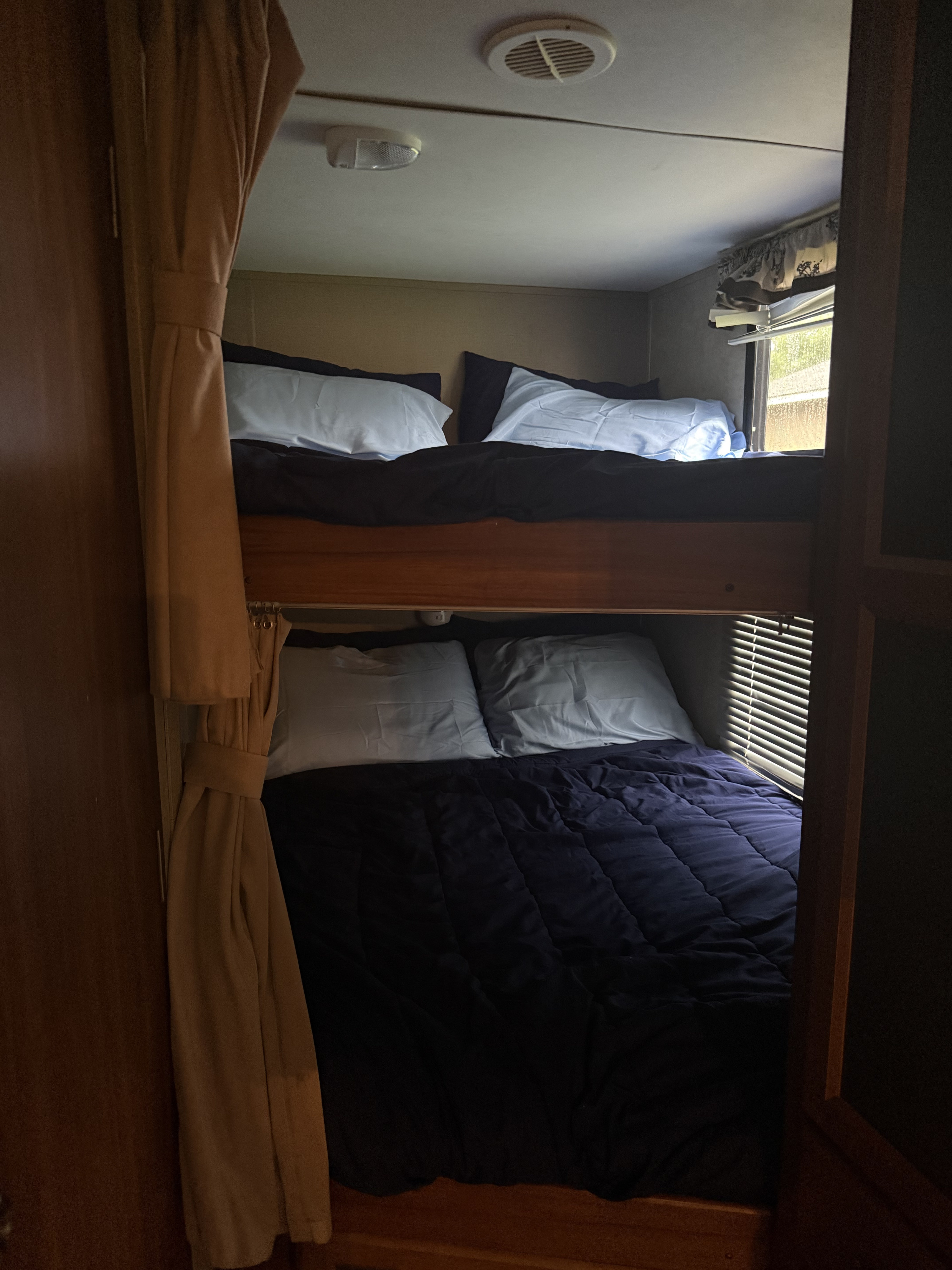 A view inside an RV rental reveals two comfortable bunk beds with dark bedding, perfect for family camping trips.. Keystone RV Cougar 2014