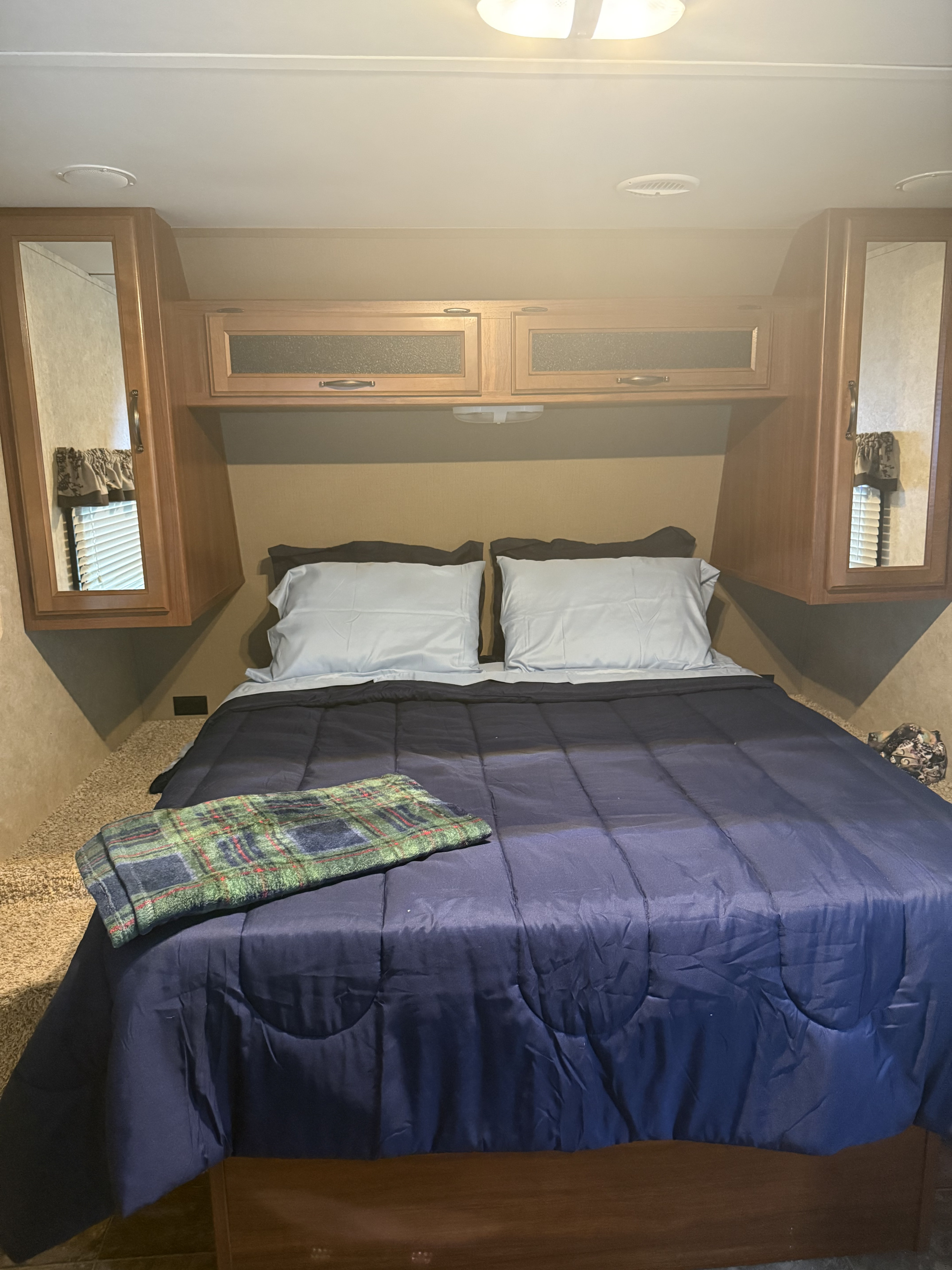 An RV rental's inviting bedroom features a neatly made bed, plaid blanket, and practical overhead storage.. Keystone RV Cougar 2014