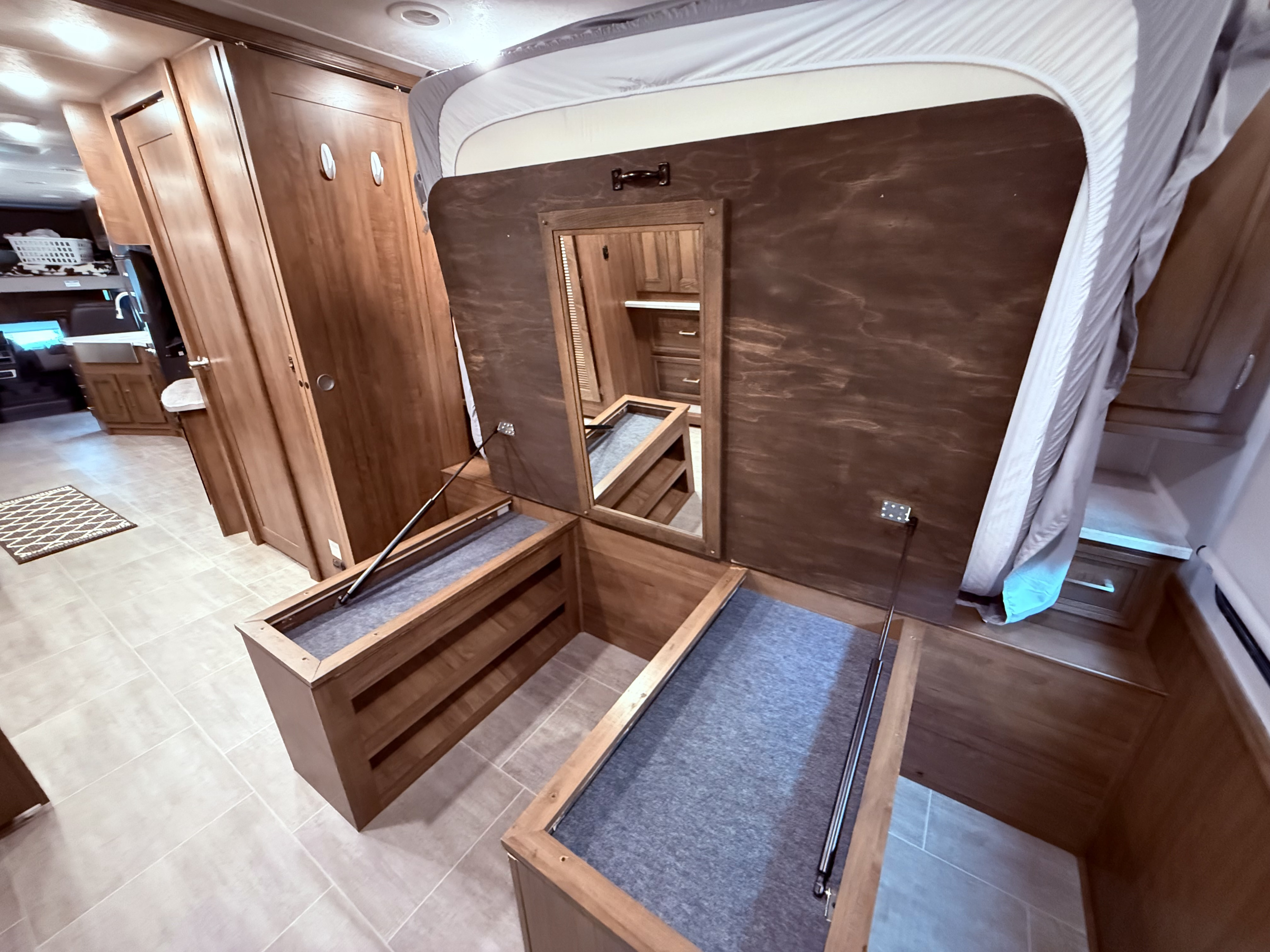RV rental bedroom: lifted bed revealing deep, carpeted storage. A mirror is integrated into the bed base, showing versatile space.. Coachman Encore 2021