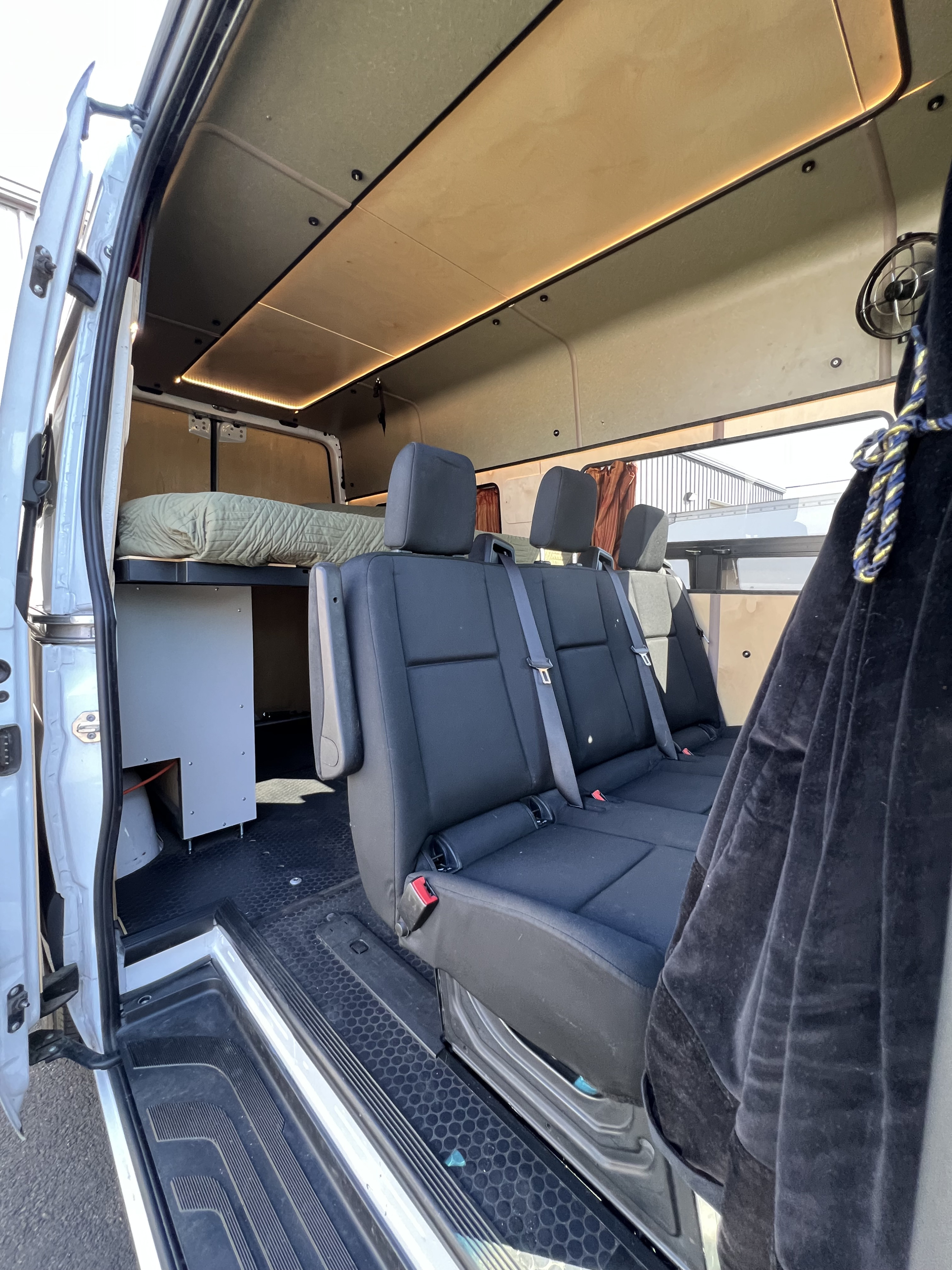 Inside a spacious RV rental camper van: passenger seating, elevated bed, and ambient lighting for road trips.. Mercedes-Benz Sprinter 2021