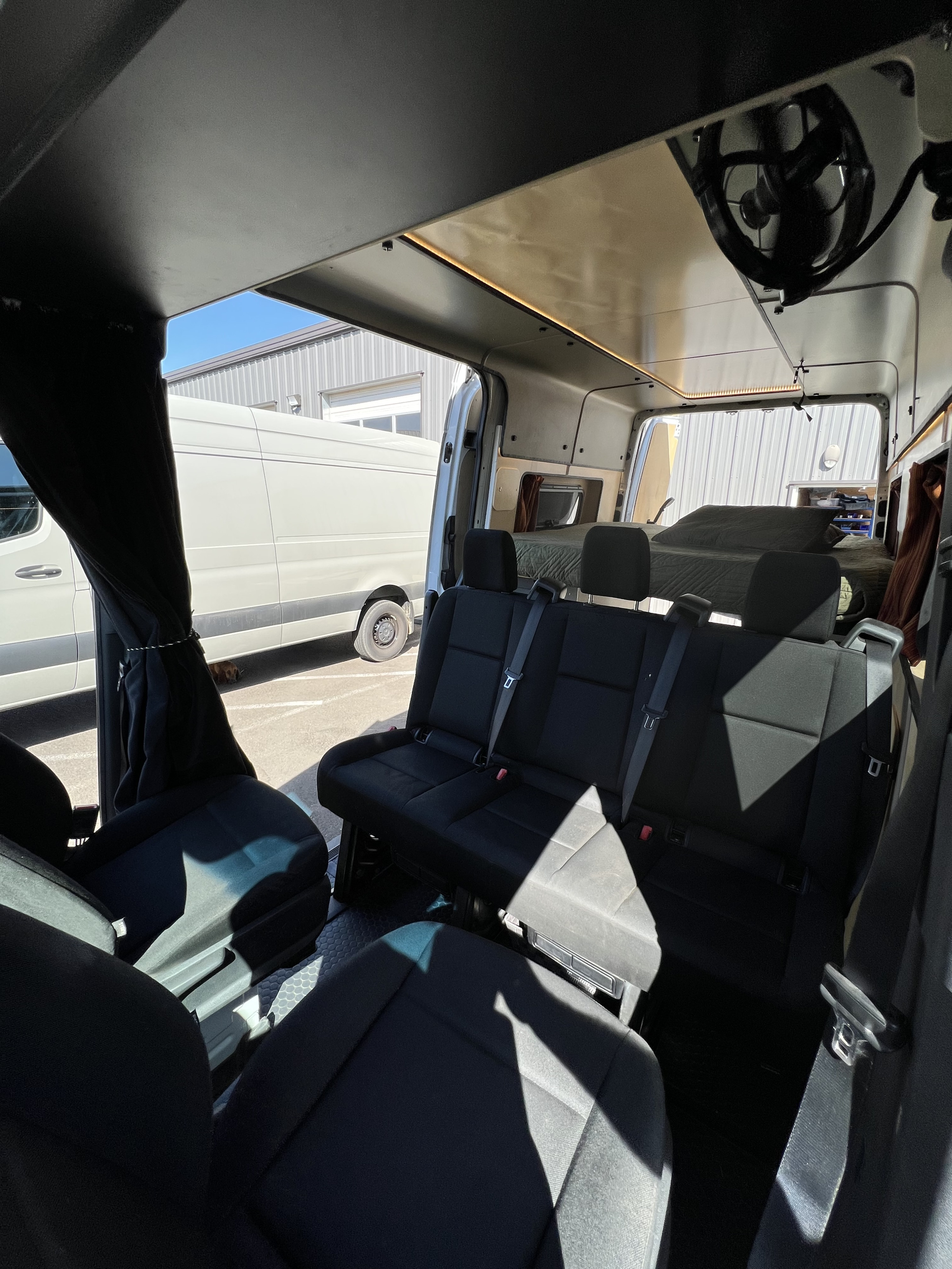View inside a modern RV rental camper van showing three passenger seats, custom ceiling lighting, and a rear bed area.. Mercedes-Benz Sprinter 2021