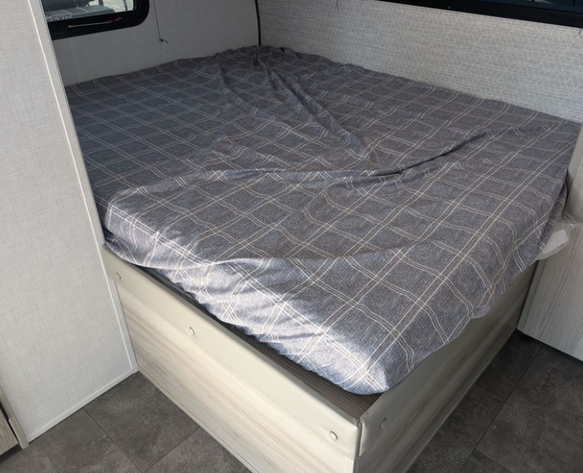 Cozy RV rental bedroom: a bed with a grey plaid sheet, light interior, and window for your next adventure.. Forest River Salem 2025