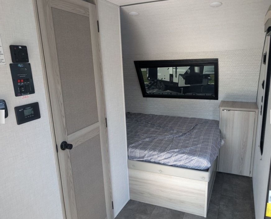 Compact RV rental bedroom featuring a window, comfortable bed, and accessible control panels on the adjacent wall.. Forest River Salem 2025