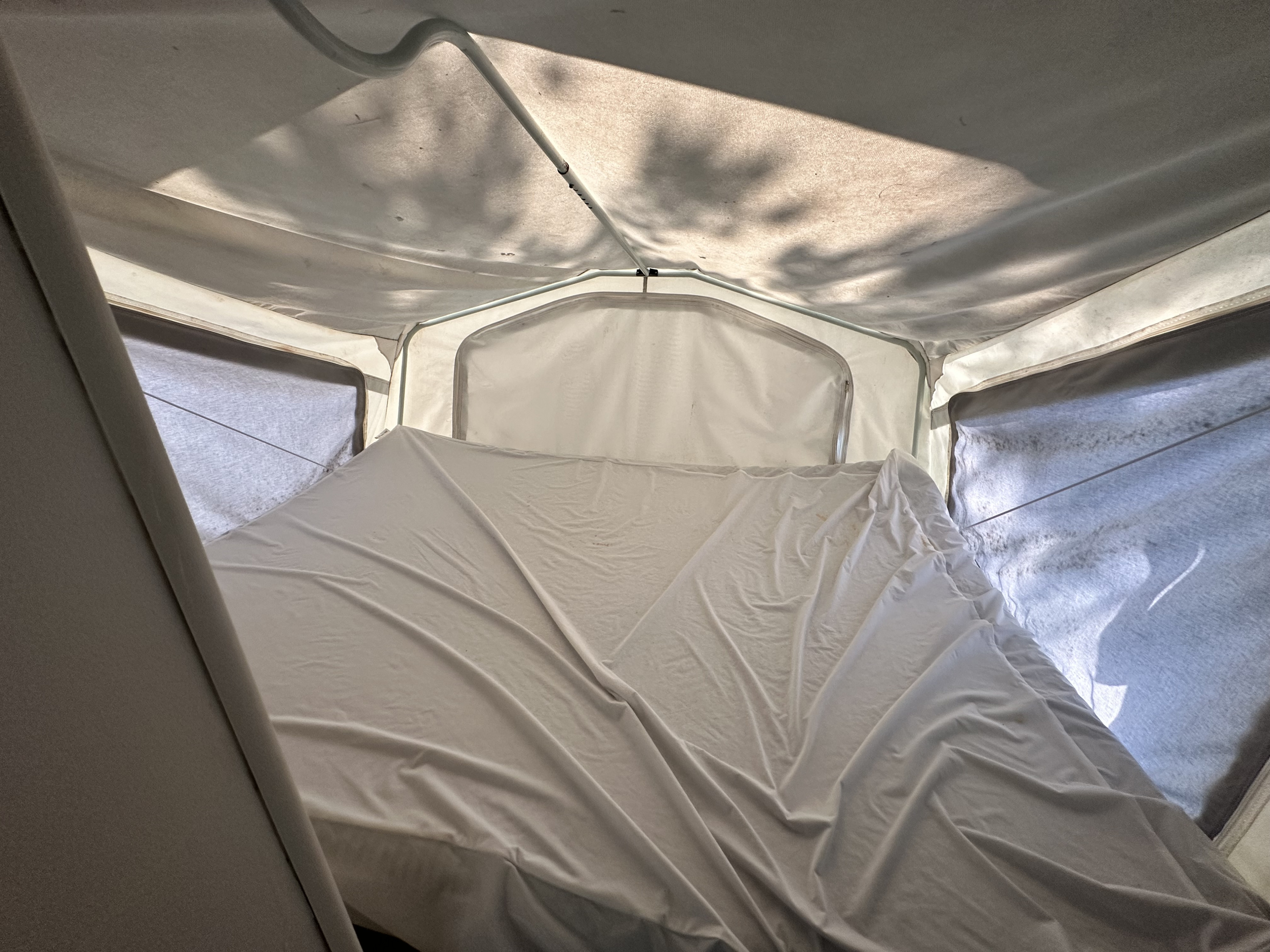 Inside a bright RV rental pop-up camper with a bed, showing the canvas ceiling, support poles, and sunlight streaming through, casting tree shadows.. Forest River Palomino Stampede 2007