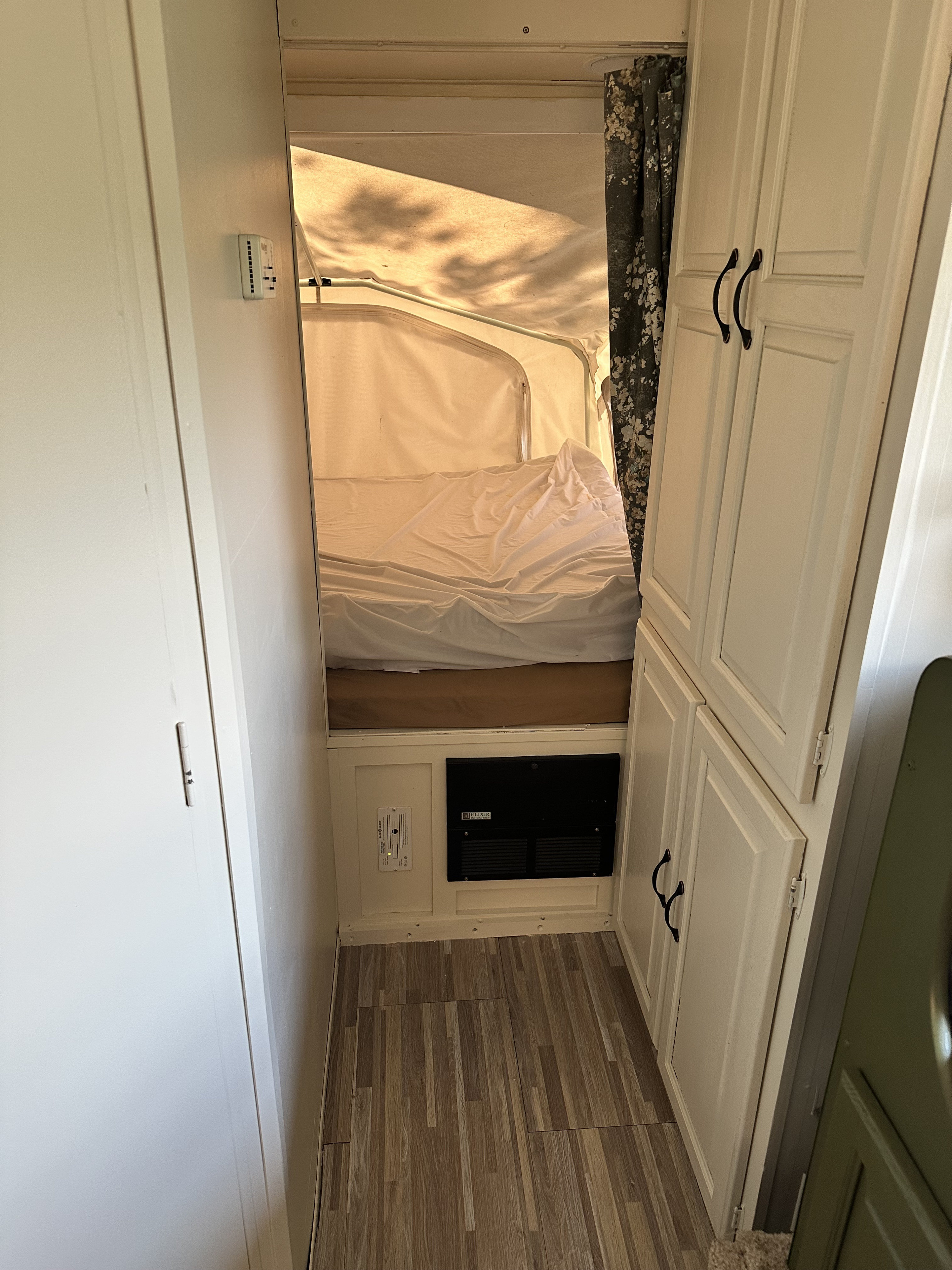 Inside an RV rental: compact space with a pop-up bed, storage cabinets, thermostat, and safety detectors.. Forest River Palomino Stampede 2007
