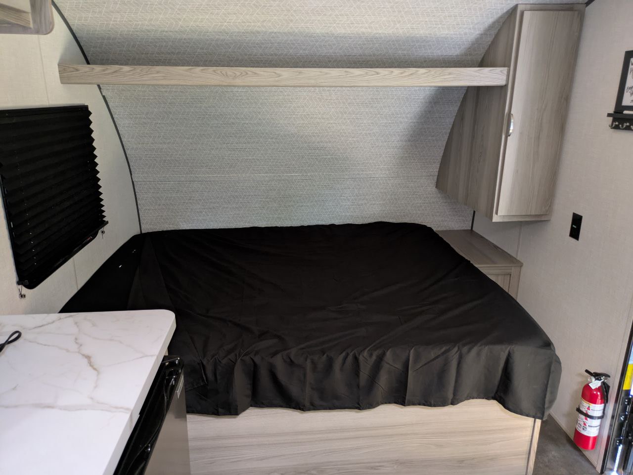 RV rental bedroom with a large bed, overhead storage, window with blinds, and a fire extinguisher for safety.. ATC Wildwood 2025