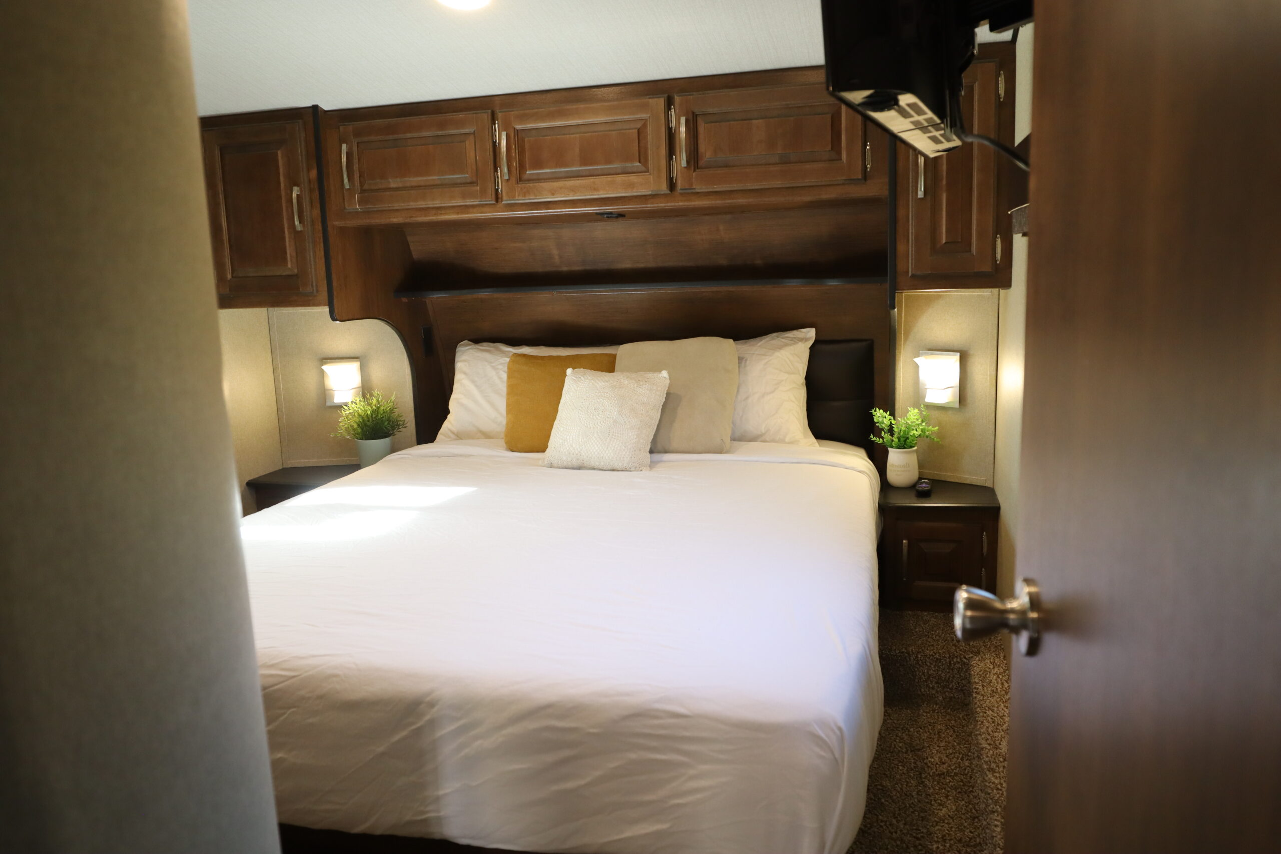 Inviting RV rental bedroom: large bed, integrated wood storage, bedside lighting, and plush carpet for a cozy retreat.. Grand Design Reflection 2019