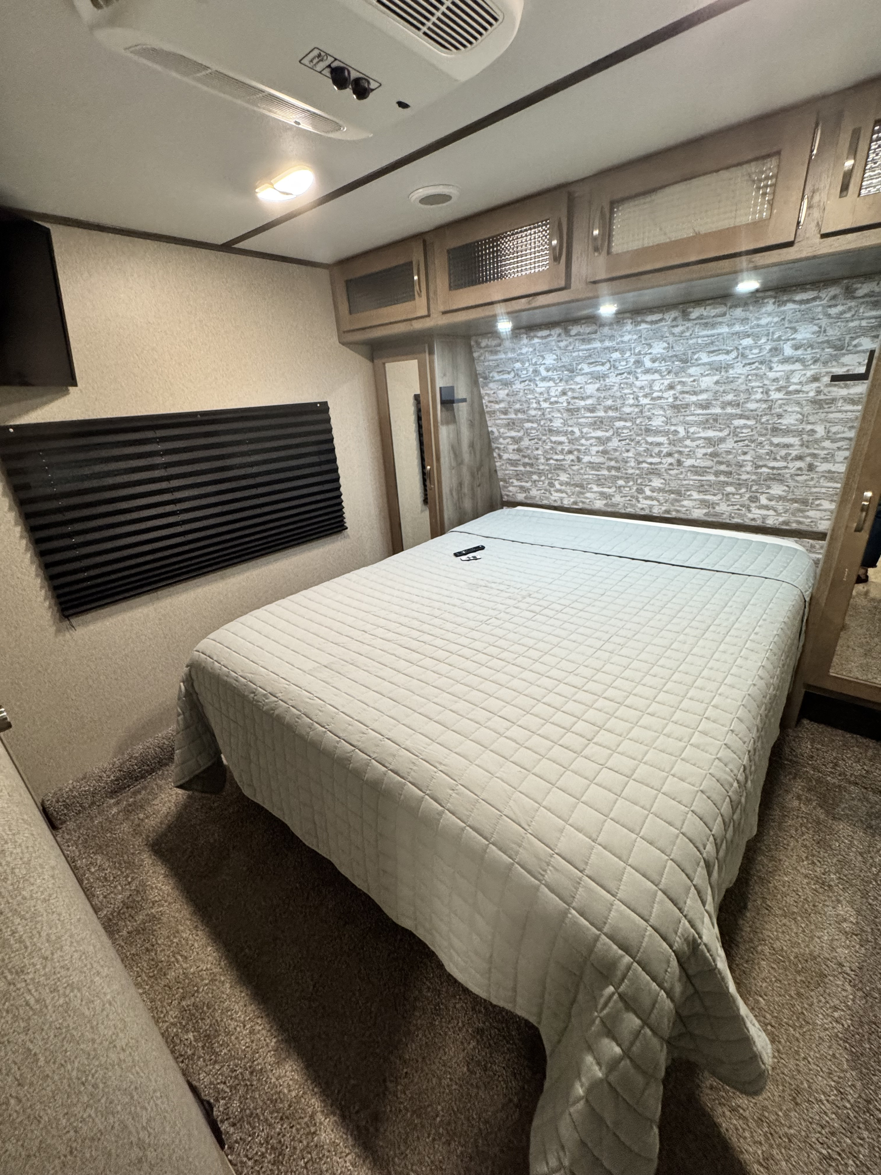 Experience comfort in this RV rental bedroom: features a cozy bed, textured wall, overhead storage, and AC for a great stay.. Keystone RV Sprinter Campfire Edition 2020