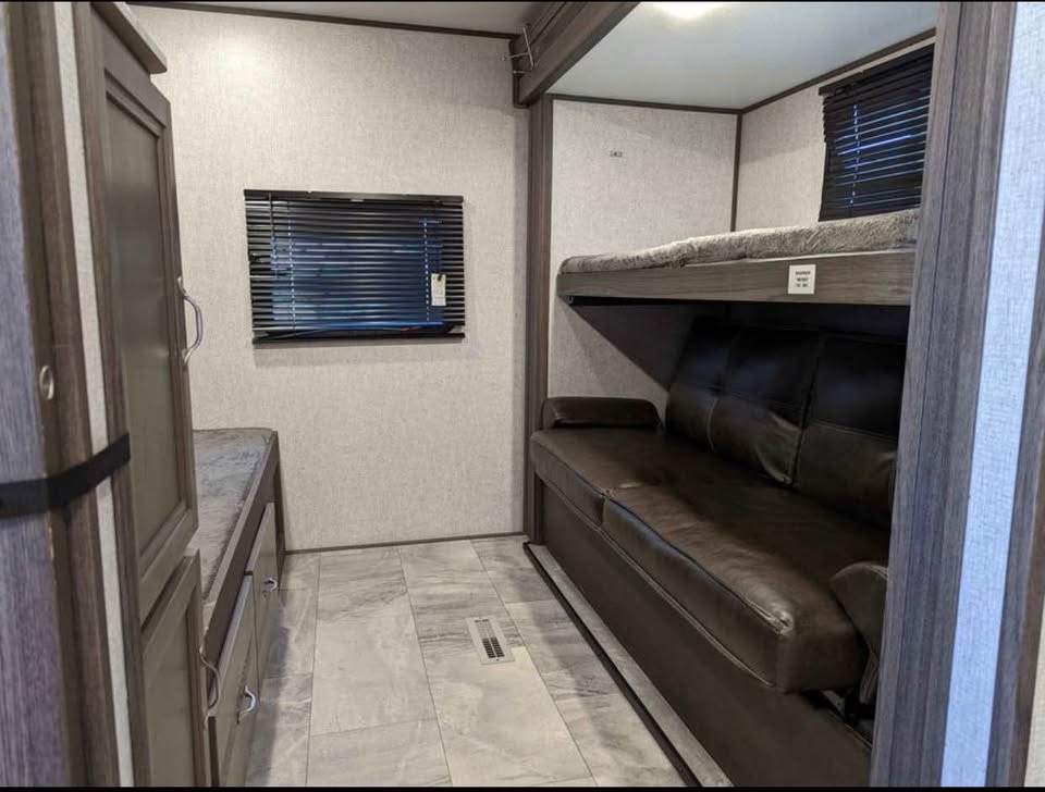 RV rental interior: A compact bunk bed area with a sofa beneath the top bunk, storage cabinets, and a window.. Dutchmen Kodiak Ultra Lite 2021