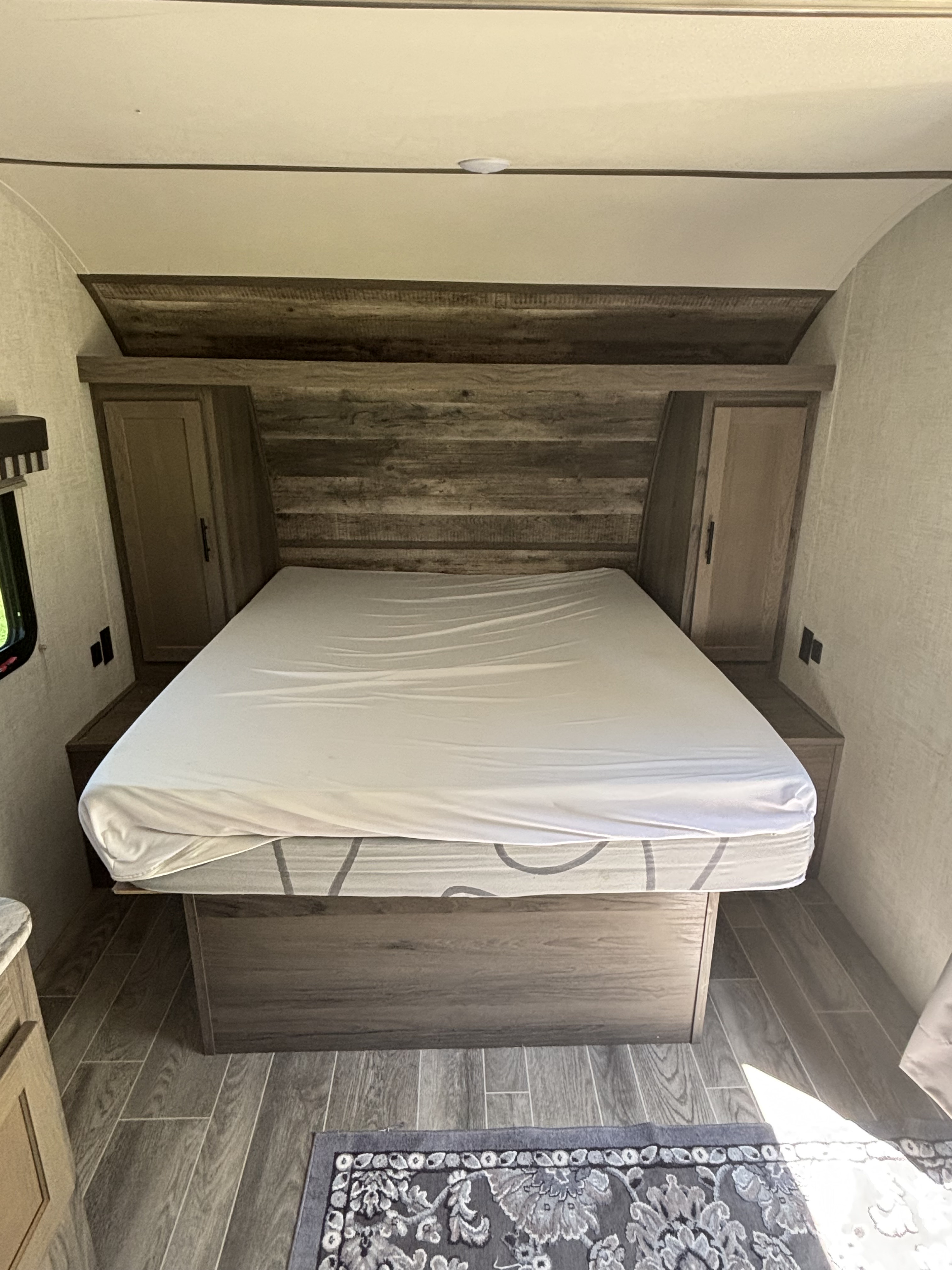 RV rental bedroom featuring a comfortable bed with rustic wood-paneled headboard and integrated side storage.. Gulf Stream Enlighten 2021